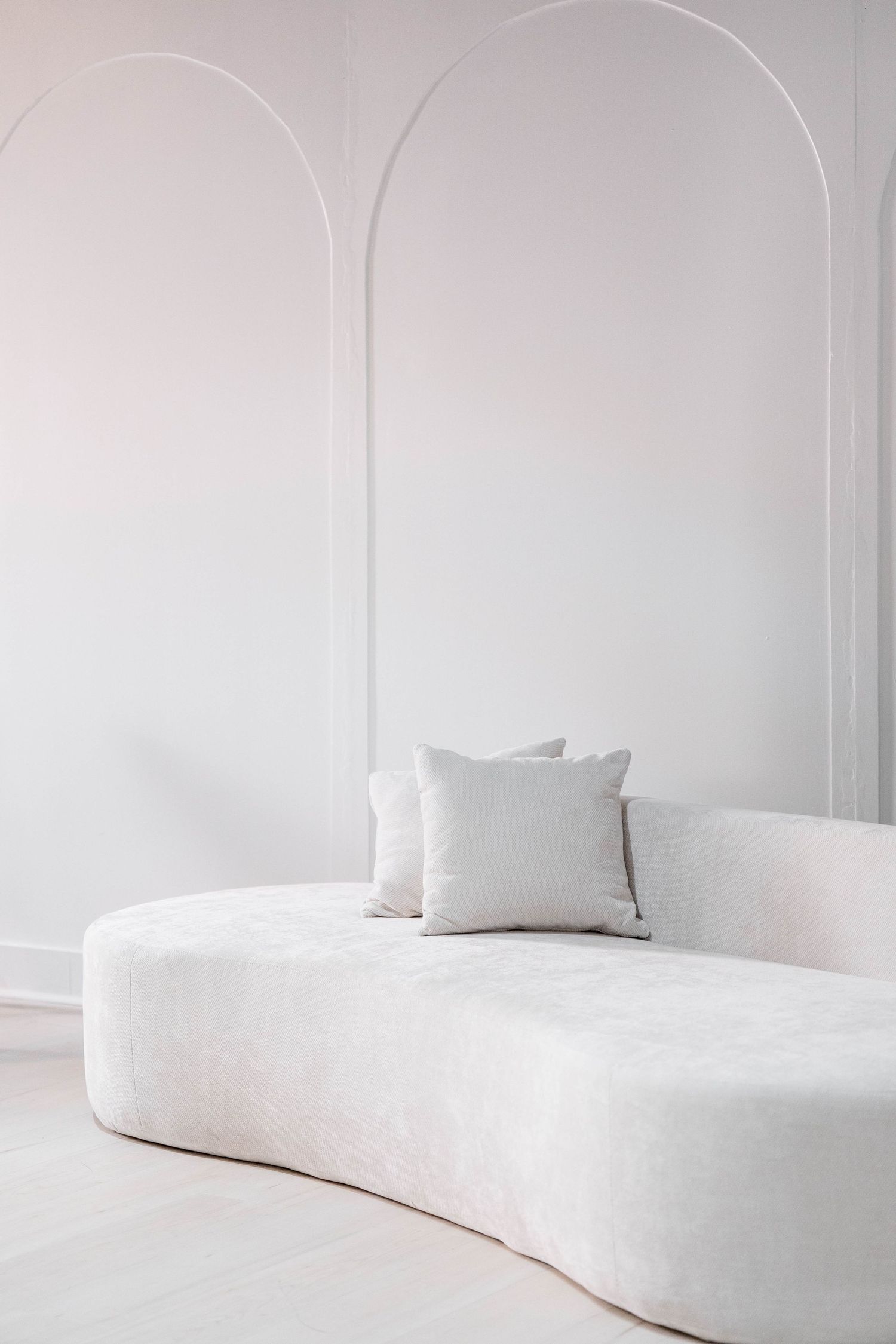 Modern curved white sofa with cushions in a minimalist white interior space.