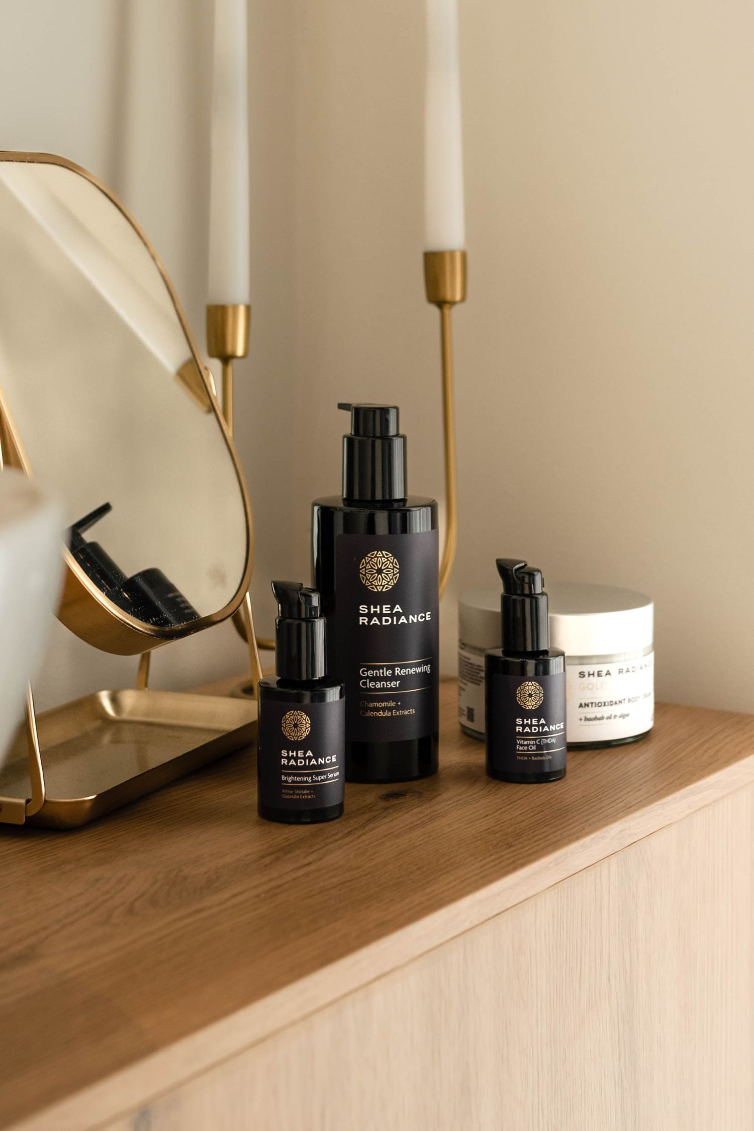 Shea Radiance skincare products displayed on a wooden vanity with a gold mirror and candle holders.