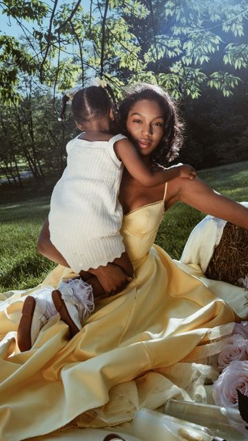Young woman in yellow satin gown sitting outdoors with a toddler on her lap near hay bales.