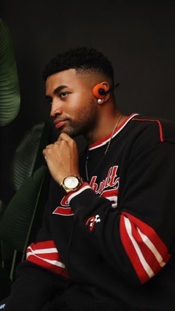 A young Black man in a Chicago Bulls jersey poses thoughtfully, wearing orange earbuds and a gold watch.