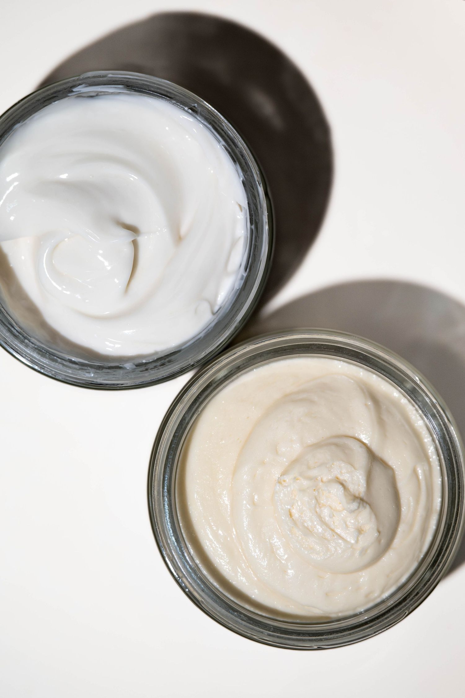 Two open glass jars of white and beige moisturizing face cream on a white background.