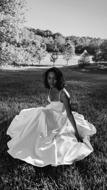 Black and white photo of a woman in a flowing white ball gown twirling in an open field.