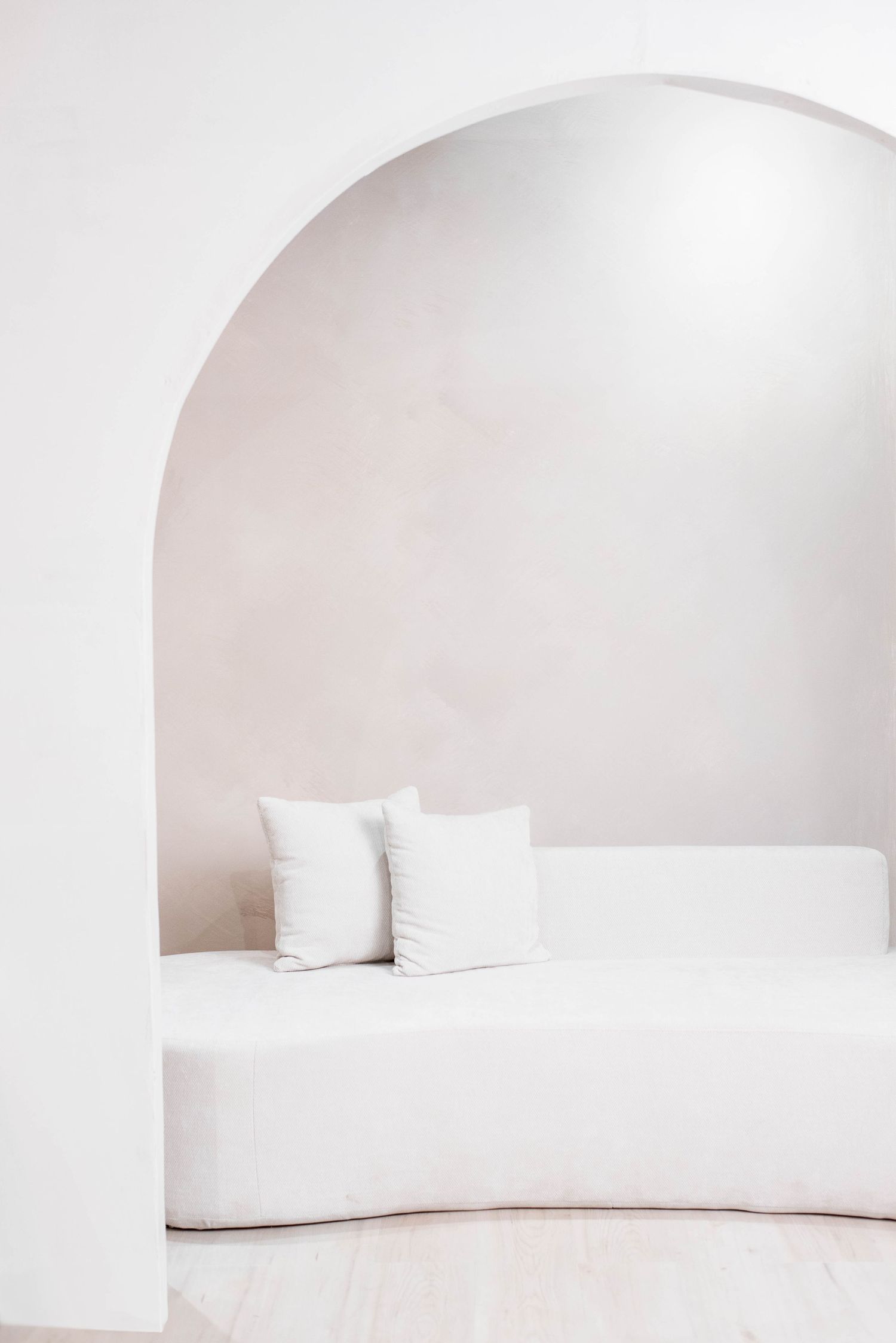 Minimalist white curved seating arrangement under an arched alcove with decorative pillows.
