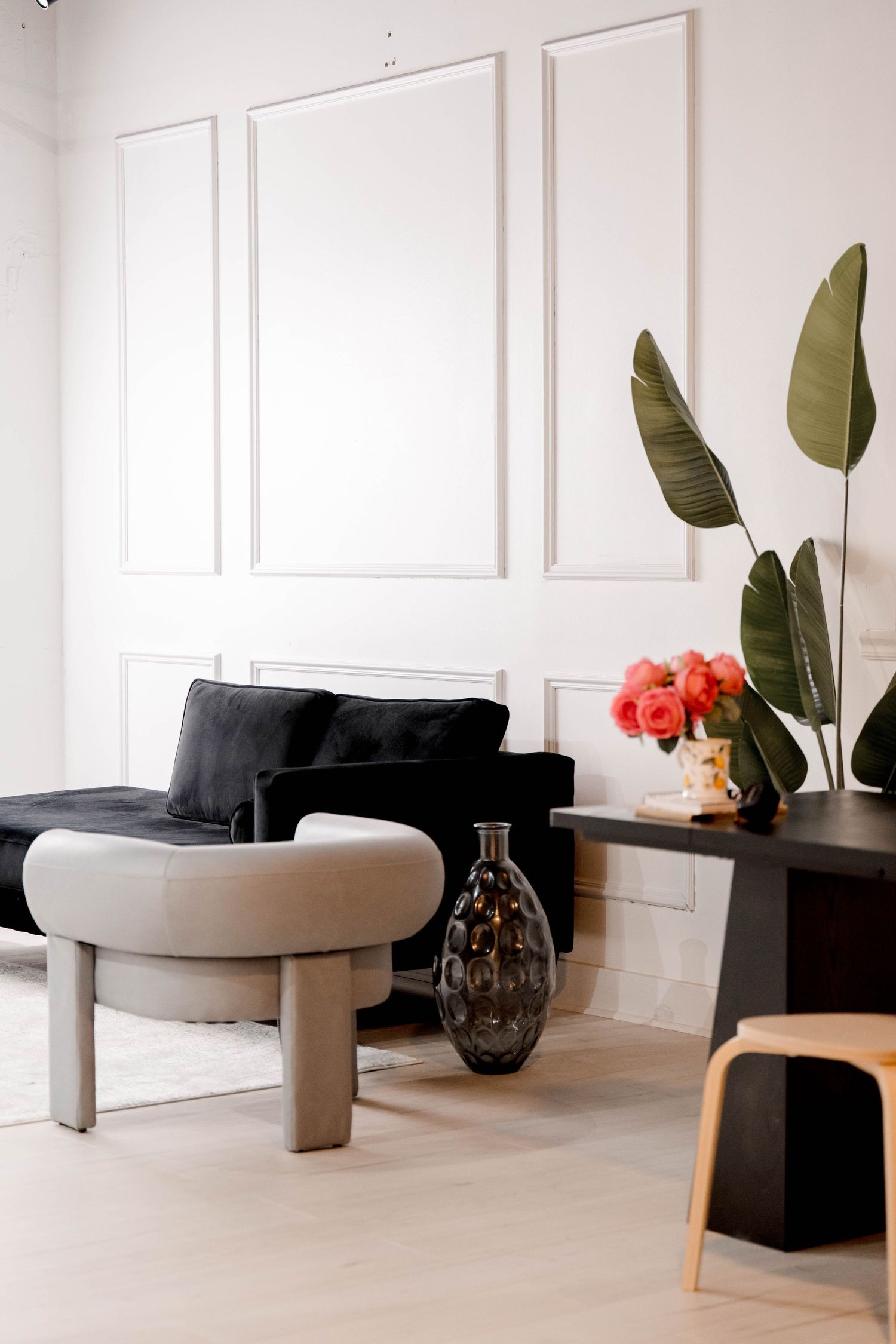 Modern lounge area with alternating black and gray seating, large leaf plants, and classic wall paneling.