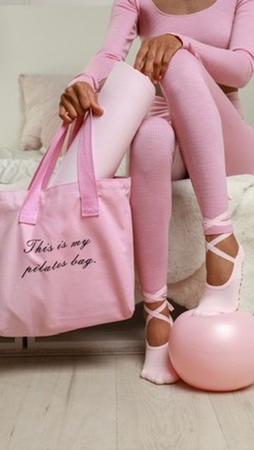 Woman in pink activewear sitting with a pink tote bag labeled This is my pilates bag and ballet flats.