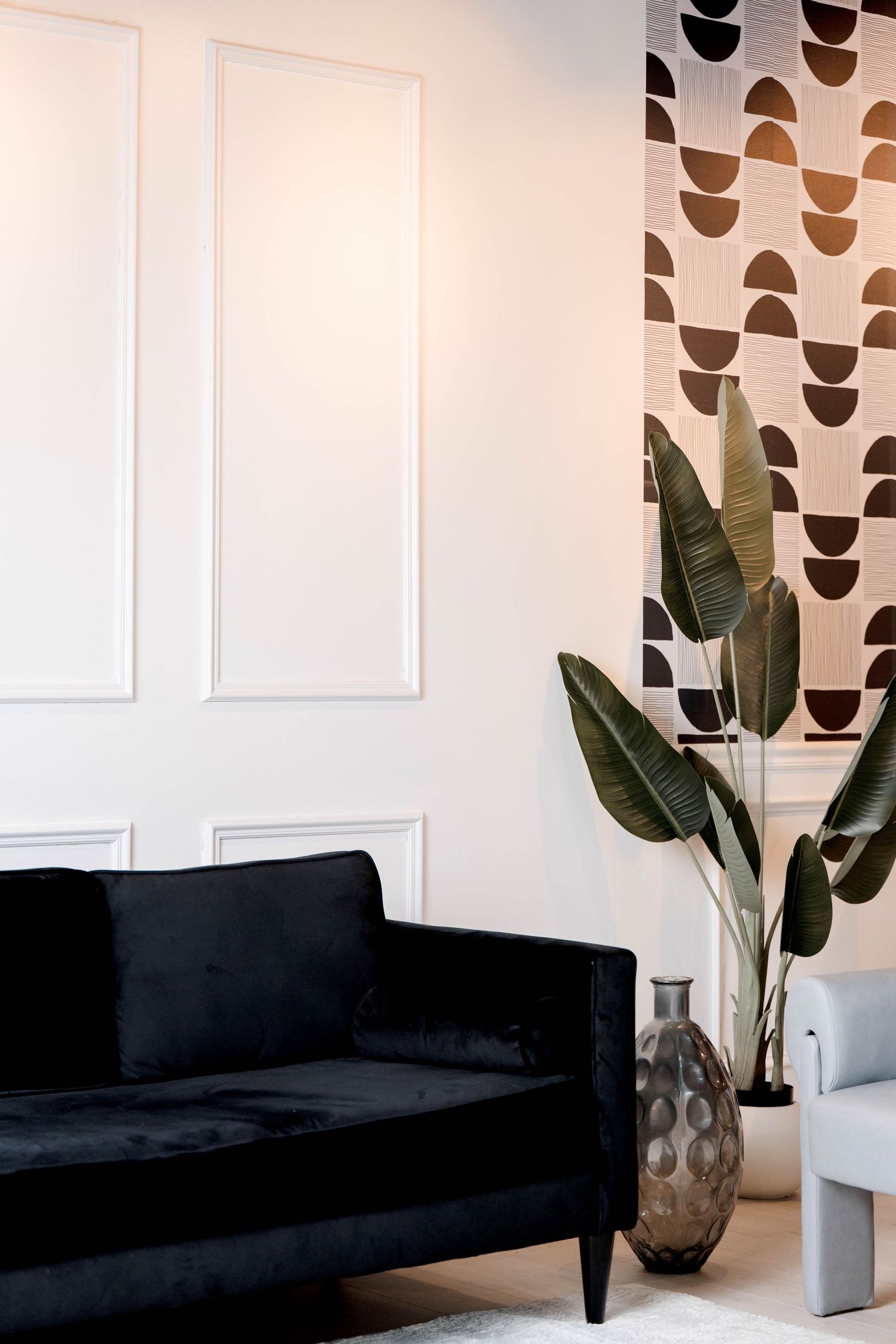 Black velvet sofa with geometric wallpaper and tropical plants in a modern living space.