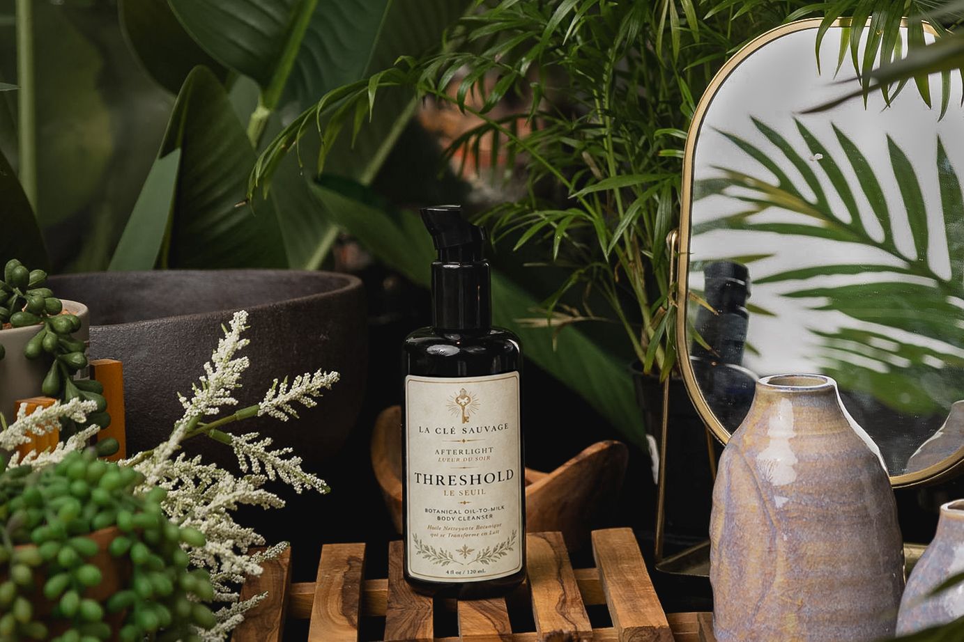 Dark botanical skincare bottle labeled Threshold displayed on wooden crate surrounded by lush tropical plants and ceramic vases.