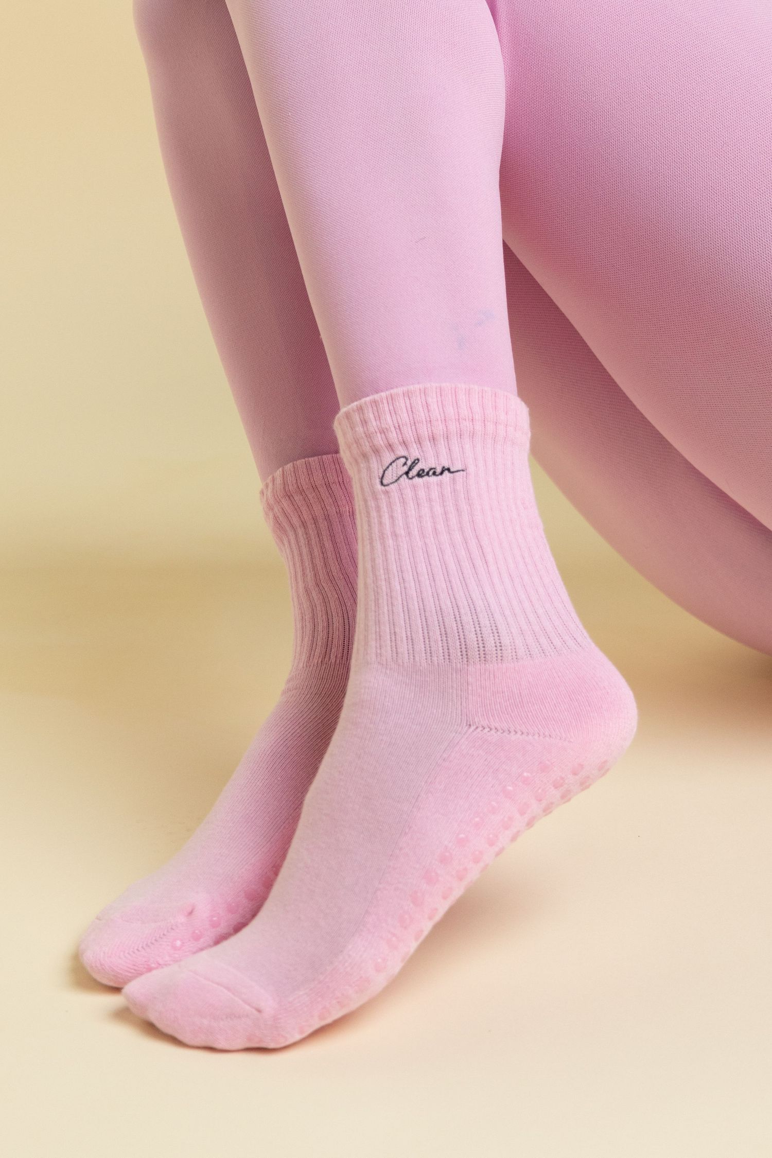 Pink ribbed ankle grip socks with cursive Clean logo, worn with matching pink leggings on yellow background.