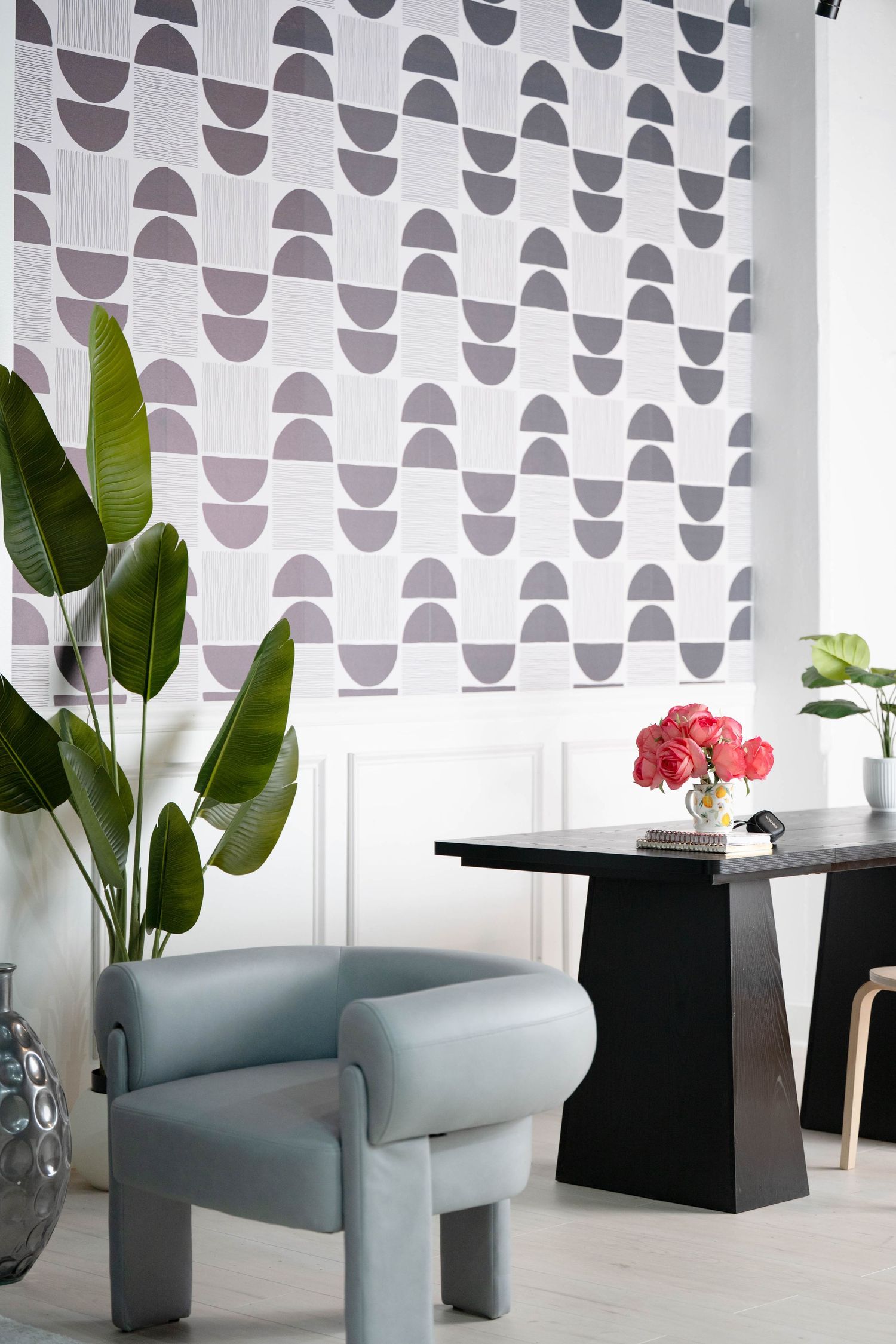Gray sculptural chairs with geometric wallpaper and tropical plants in modern space.