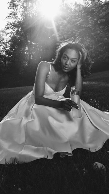 Black and white photo of a woman in a white dress sitting on grass in sunlight.