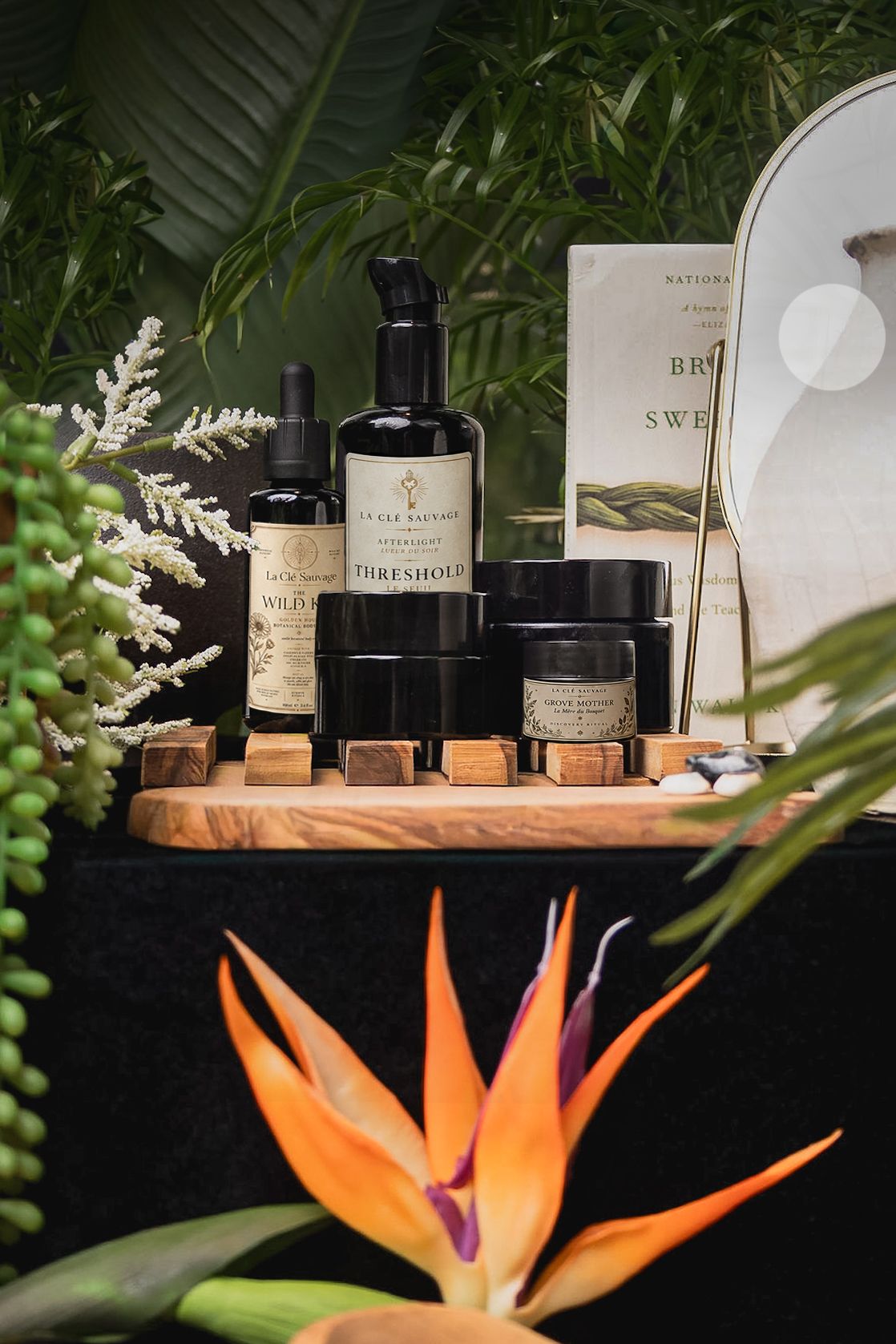 Luxury skincare products displayed on wooden tray with tropical plants and bird of paradise flower.