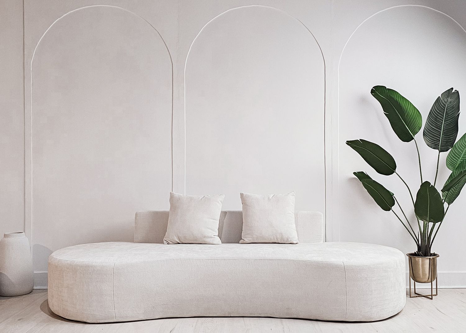 Modern white curved sofa with plush cushions and indoor plants in a minimalist living room setting.