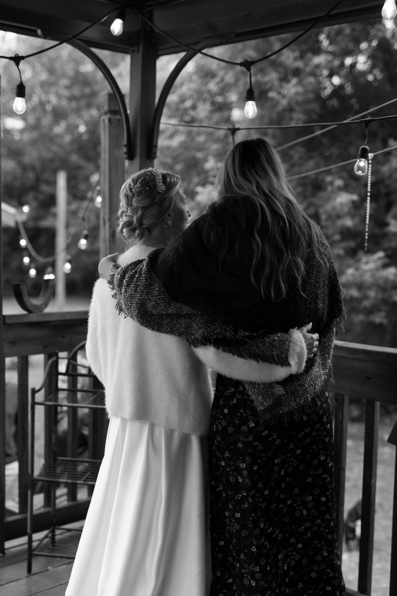 Two figures embrace on a porch decorated with string lights in black and white photograph.