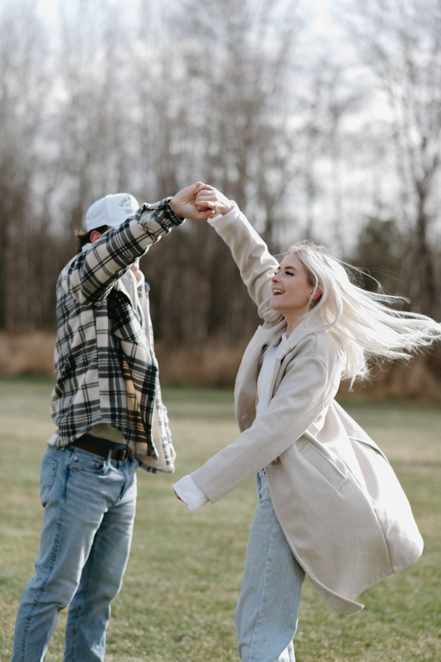 A joyful couple dancing outdoors in a field, man spinning woman with flowing blonde hair in autumn setting.