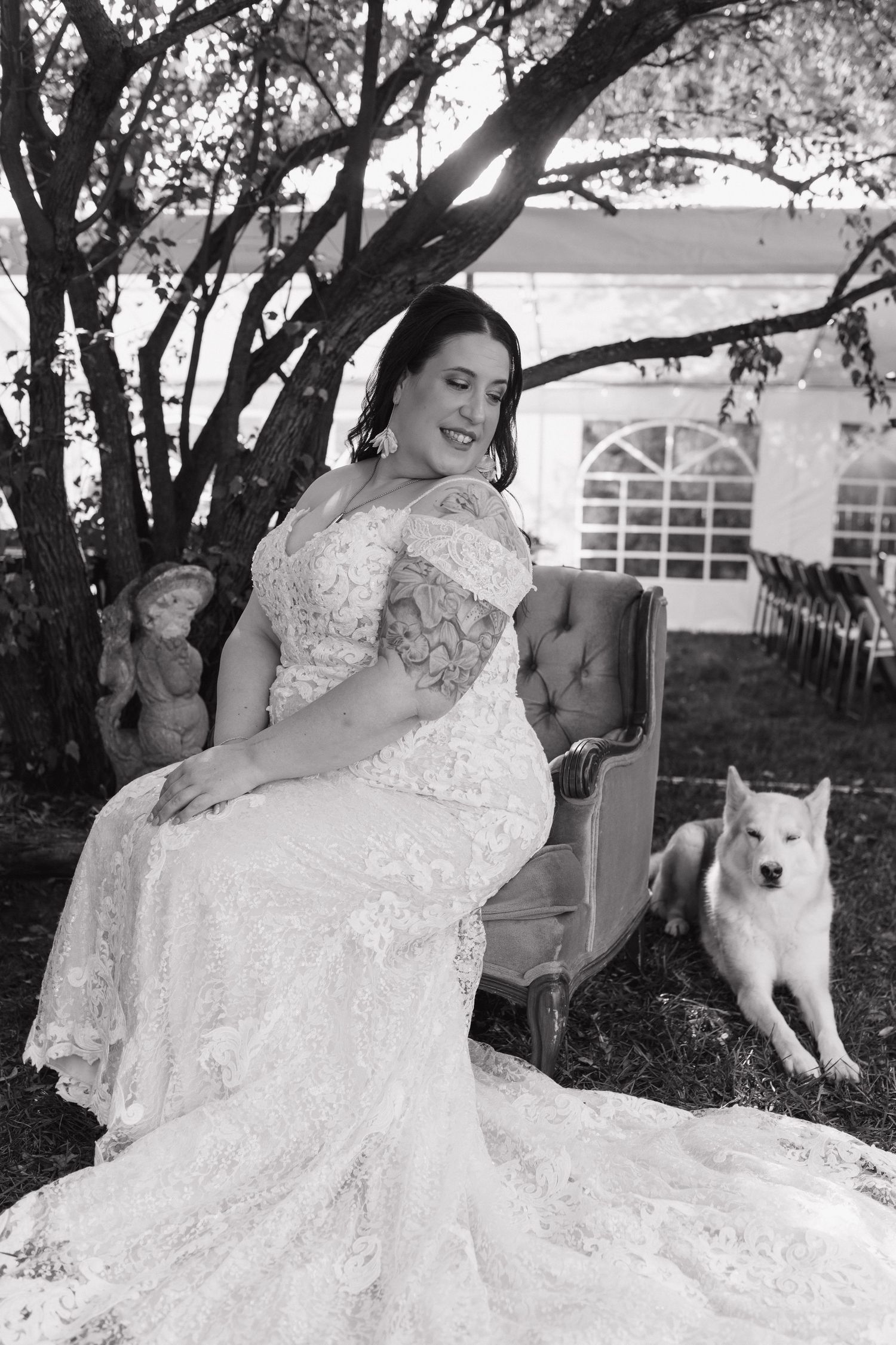 An elegant bridal portrait on a velvet settee outdoors with a white dog in the background.