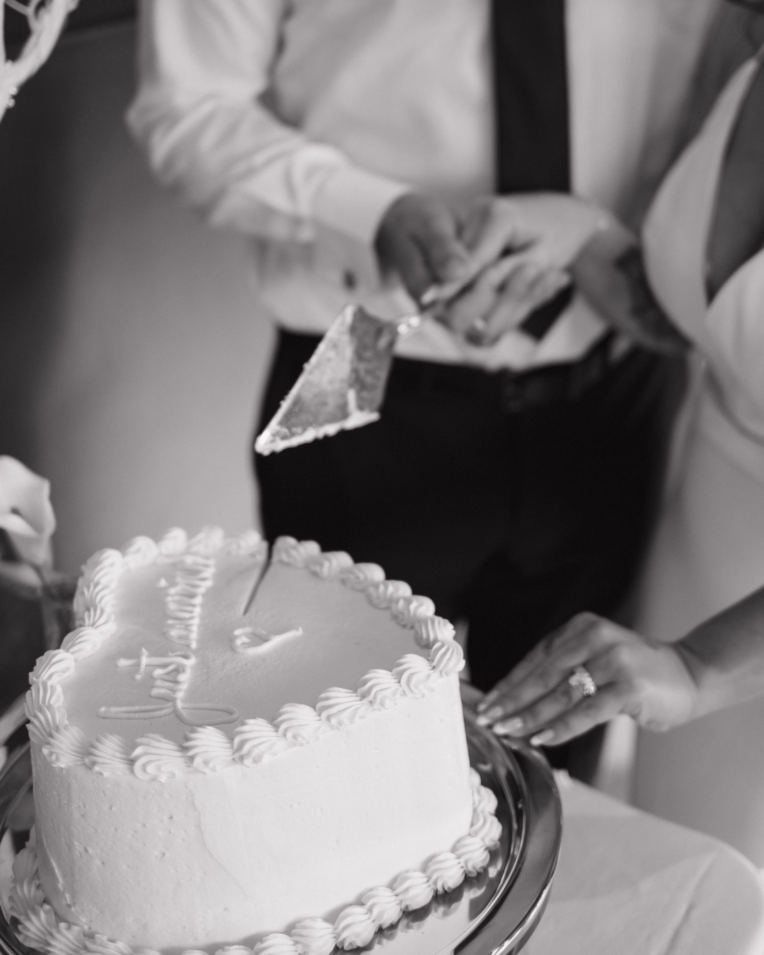 Black and white photo of hands cutting into a heart-shaped white frosted cake.