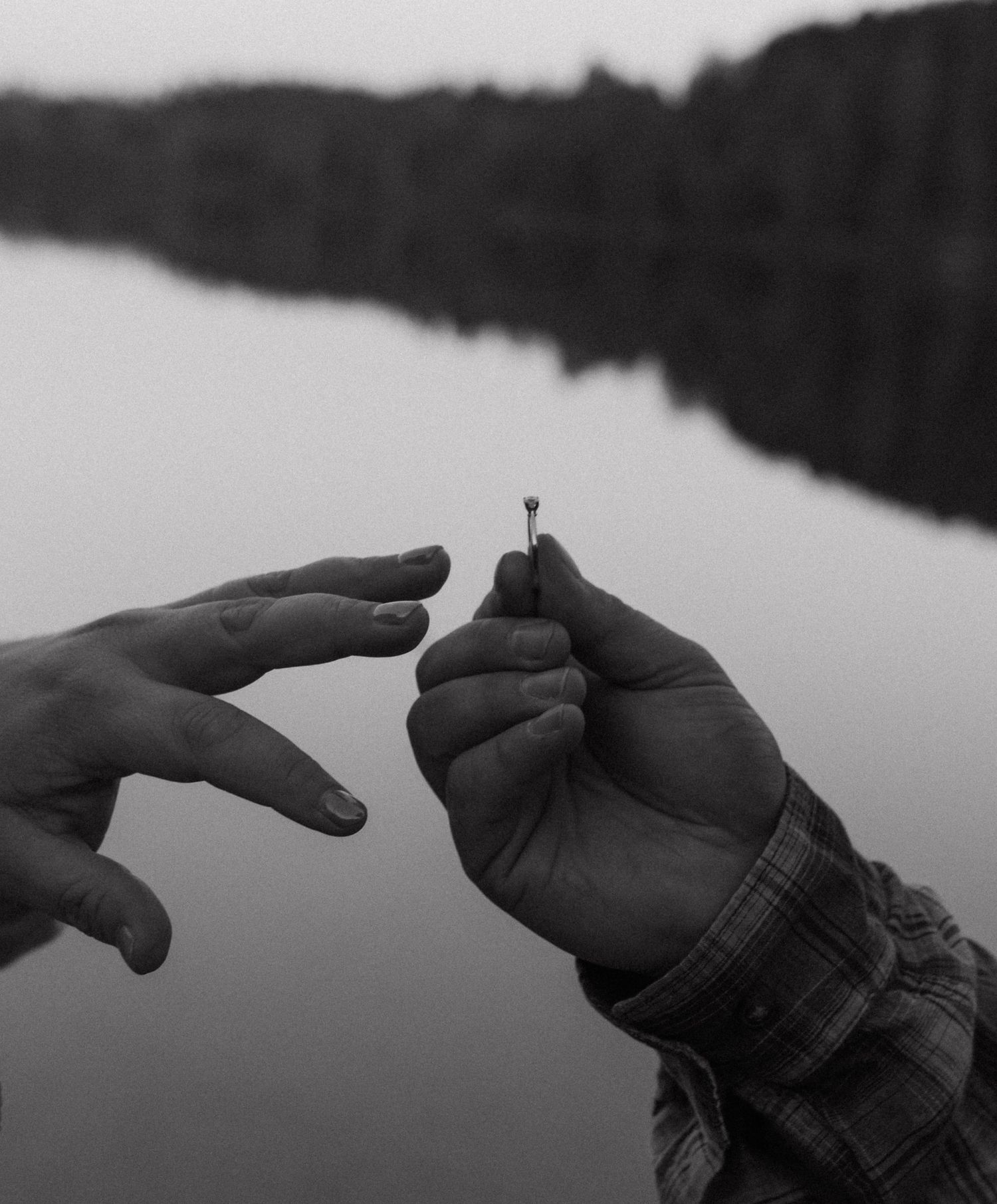 Black and white photograph of hands reaching towards each other over reflective water.