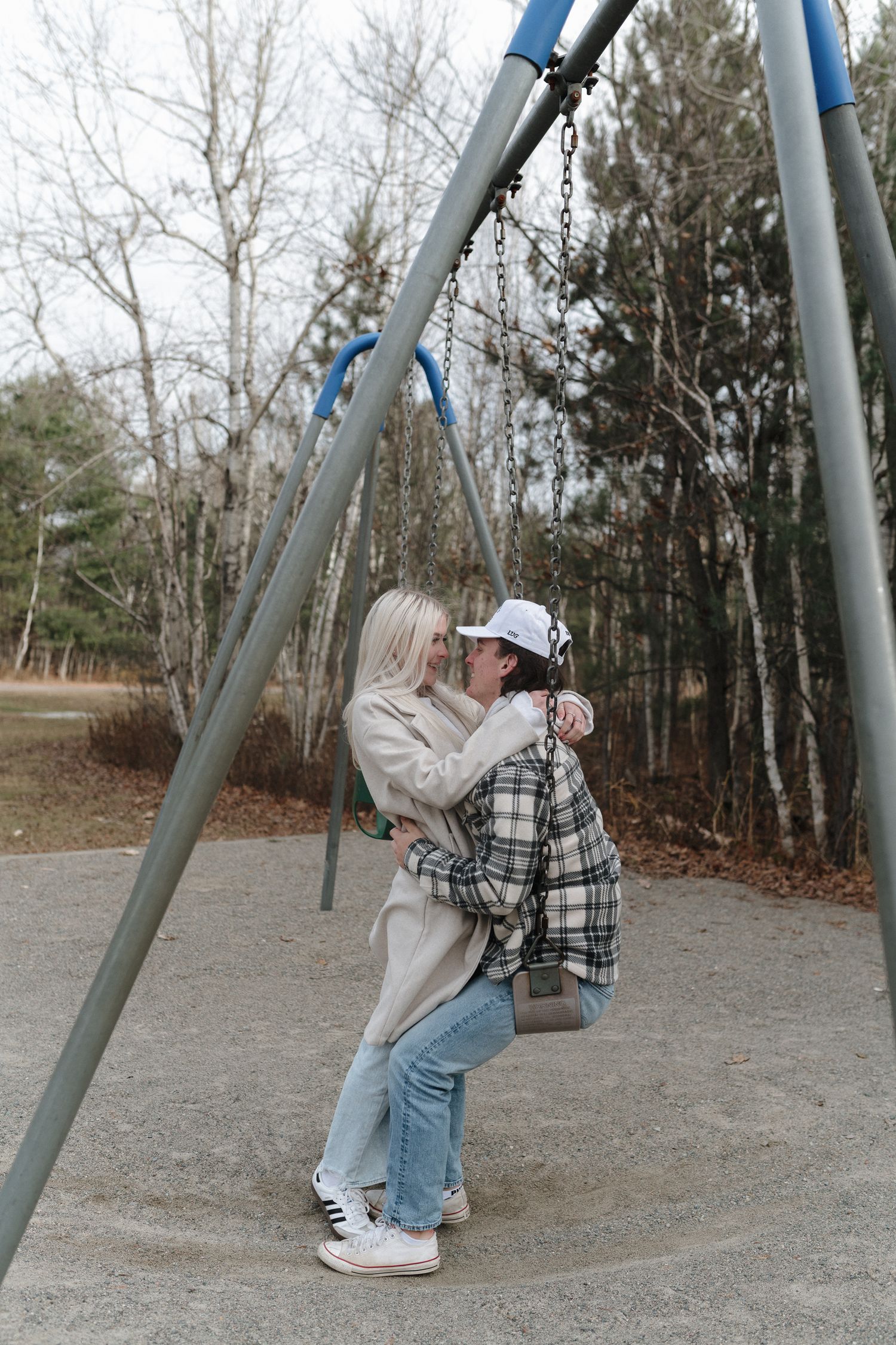 Romantic couple embracing on a playground swing set among bare autumn trees.