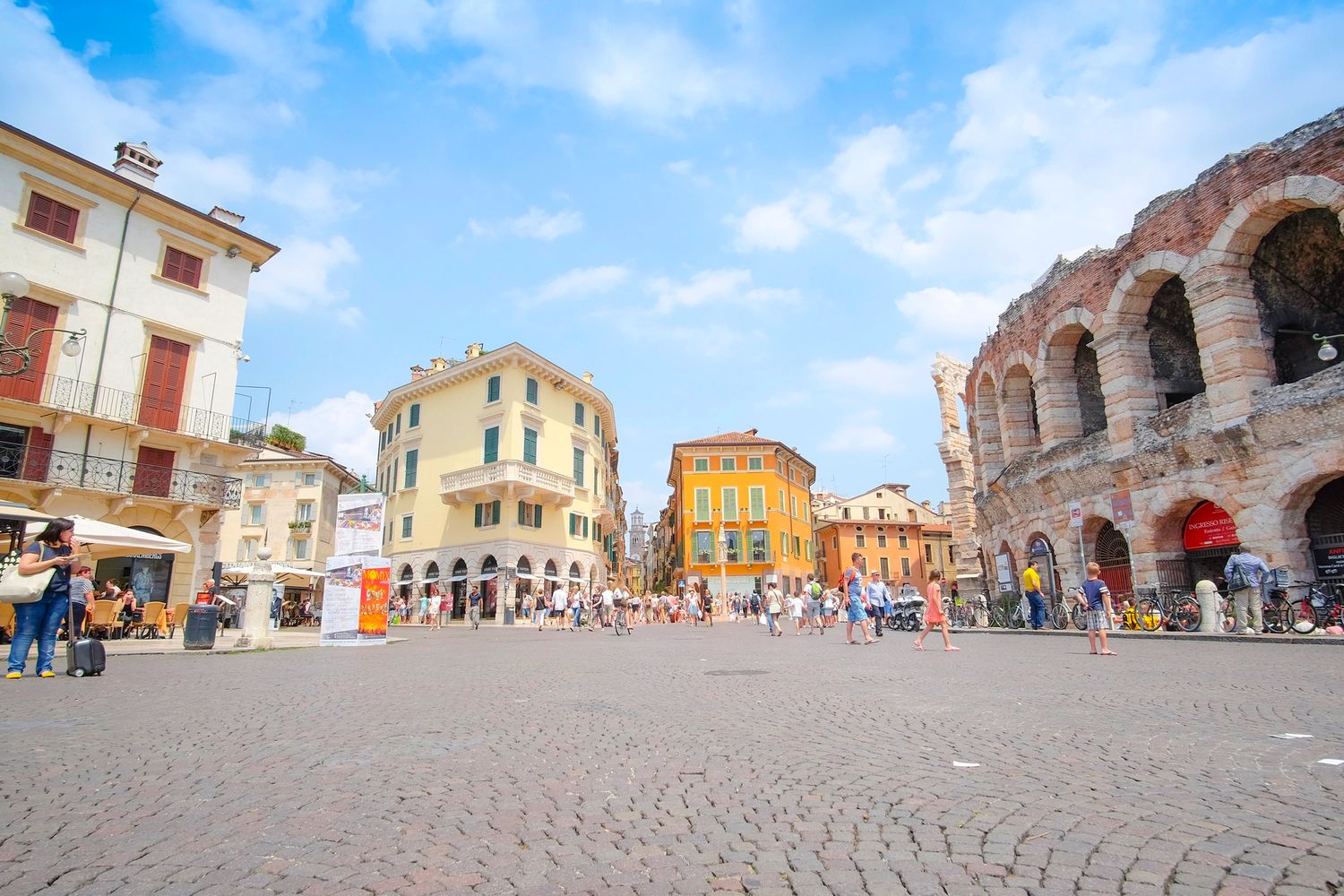 Piazza Bra in Verona, Italy, featuring the ancient Roman Arena and colorful historic buildings under a blue sky.