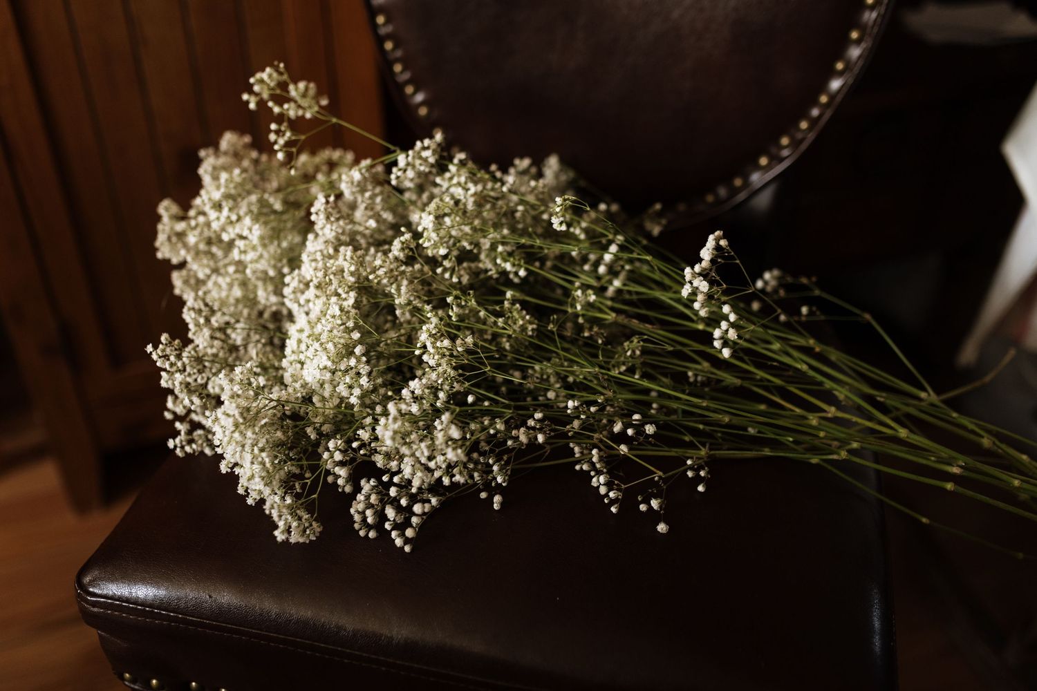 Dried baby's breath bouquet resting on a dark brown leather chair in a rustic wooden interior.
