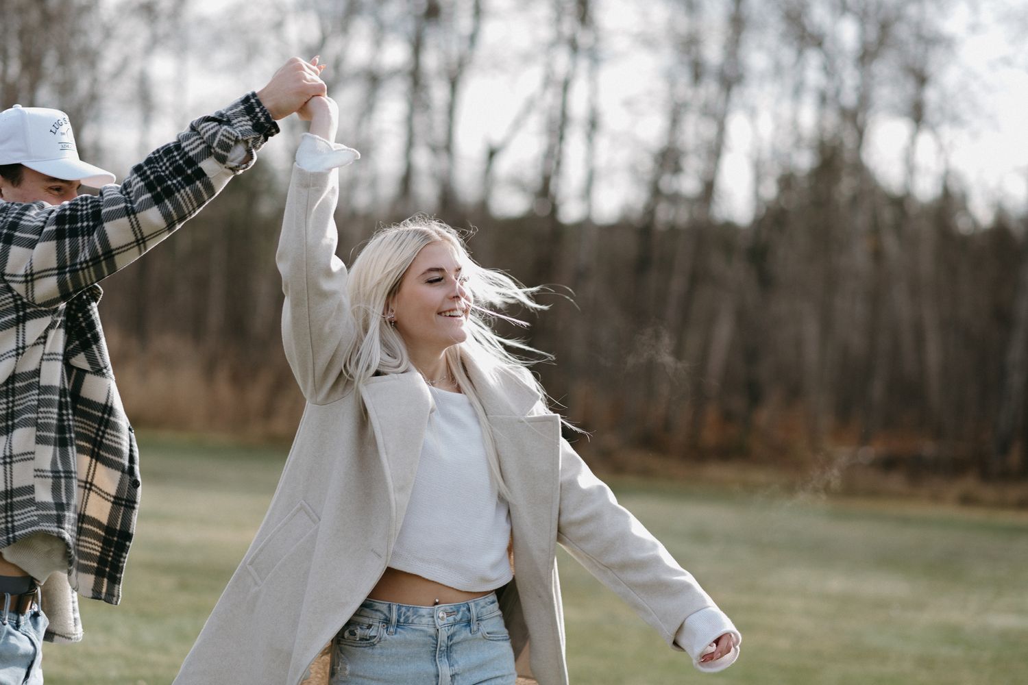 Happy blonde woman dancing outdoors with partner while holding hands in an open field.