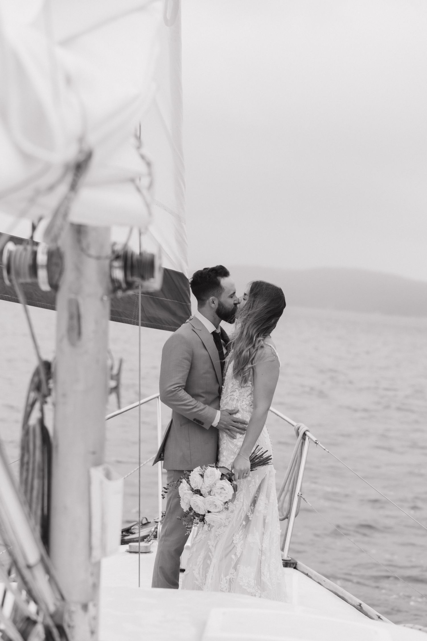 A couple embraces on the deck of a sailboat during their wedding photoshoot.