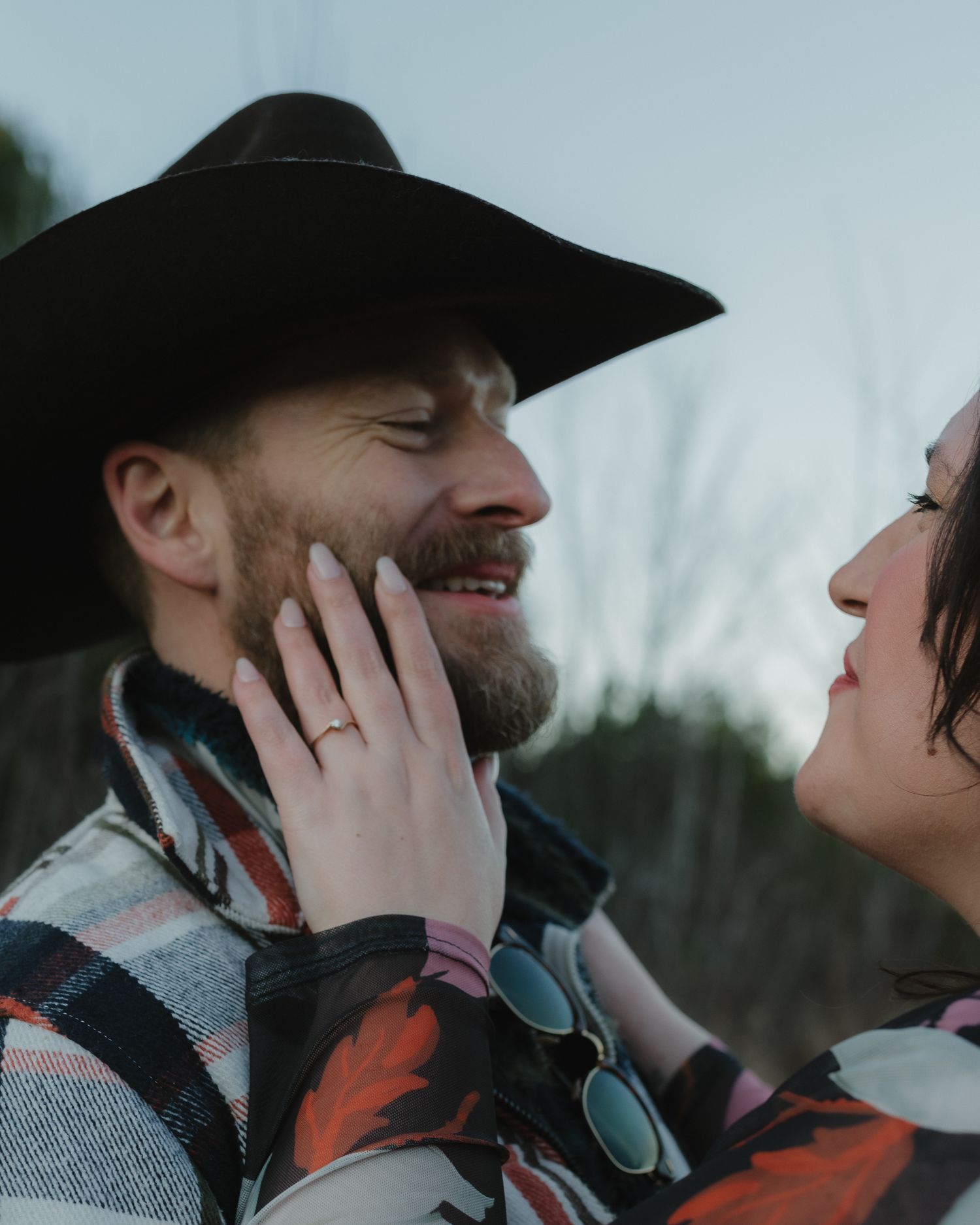 A couple shares an intimate moment outdoors while wearing winter clothing and a cowboy hat.