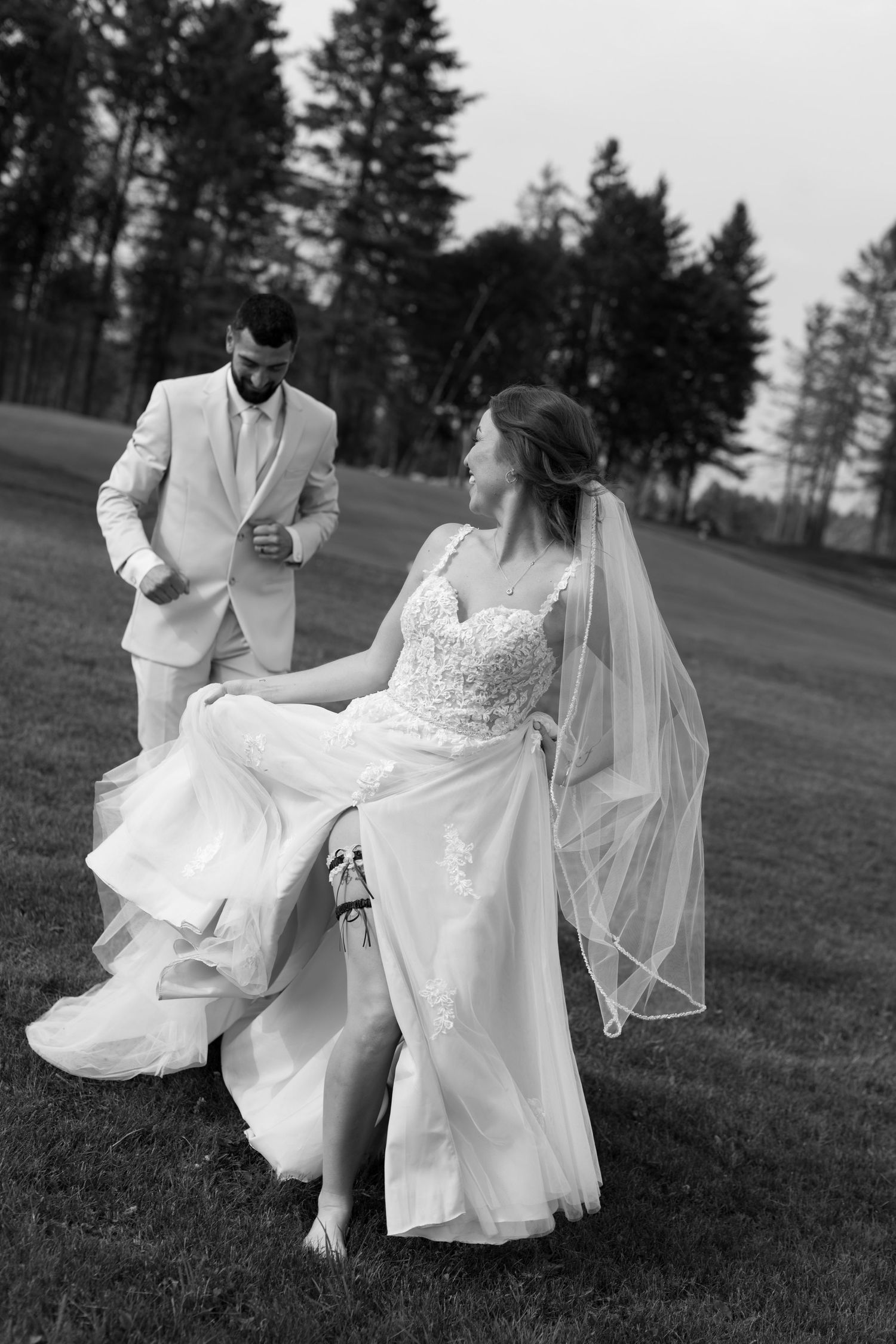 Black and white photo of a couple in wedding attire chasing each other The Iron Golf Course Chelsmford