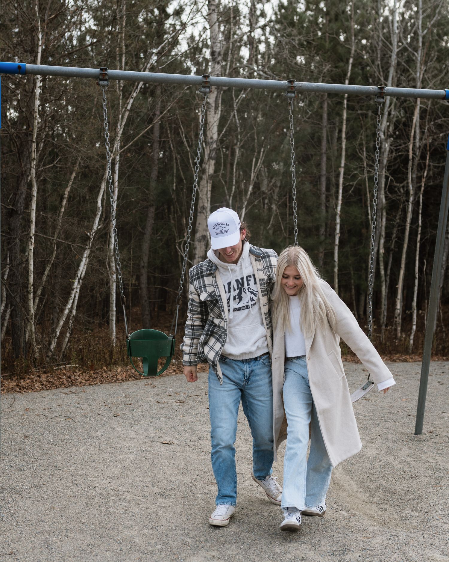 Couple walking hand in hand at a playground with bare trees in the background.