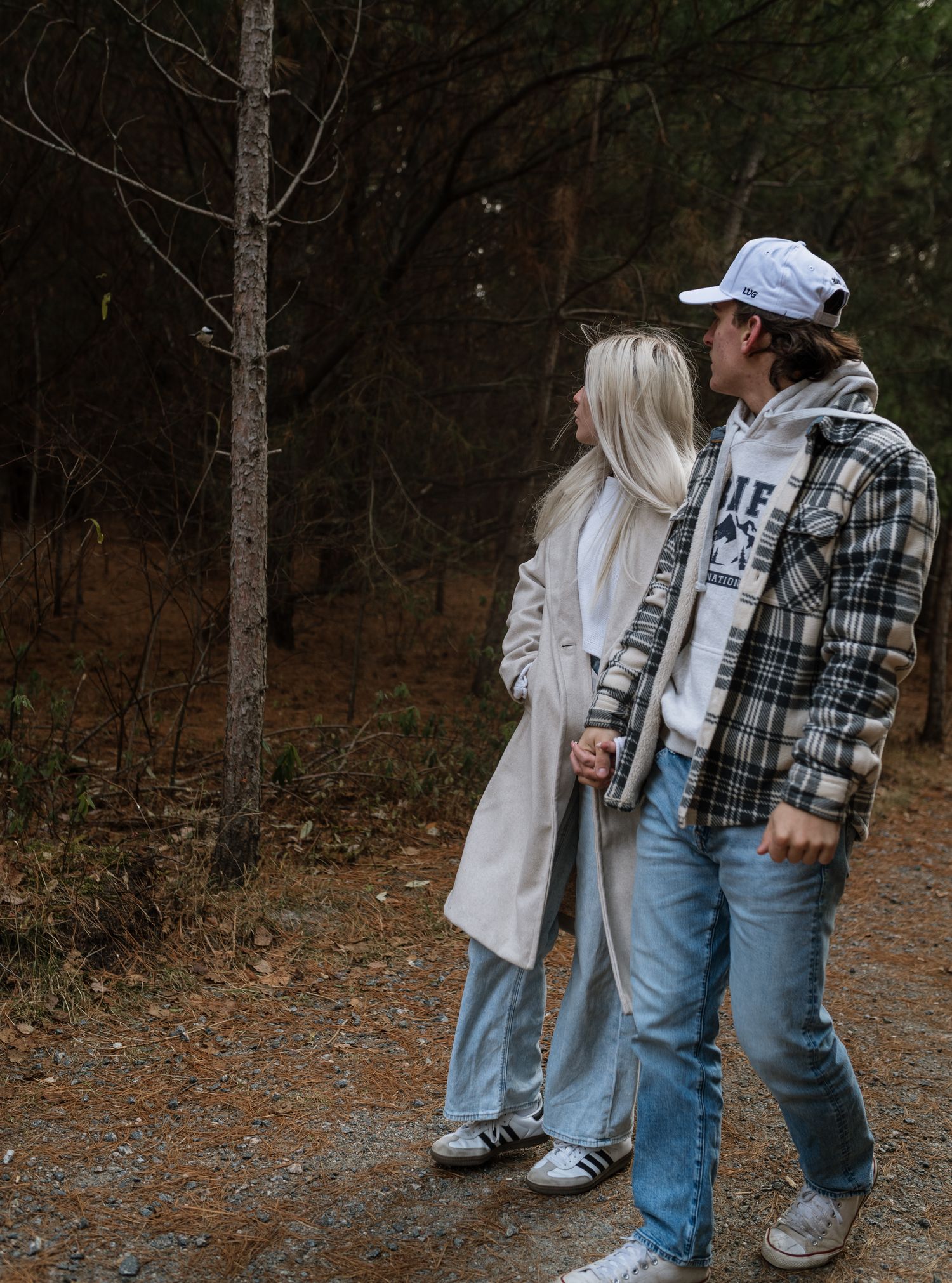 Young couple walking hand in hand on forest path in casual fall outfits.
