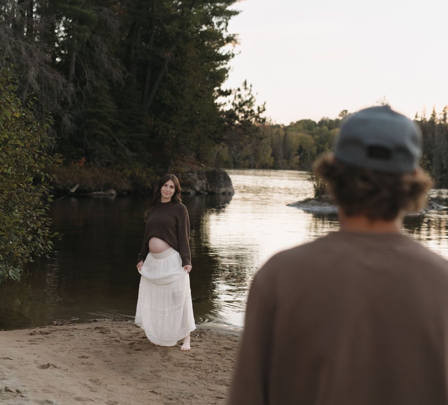 Couple enjoying sunset on beach with evergreen forest and water views.