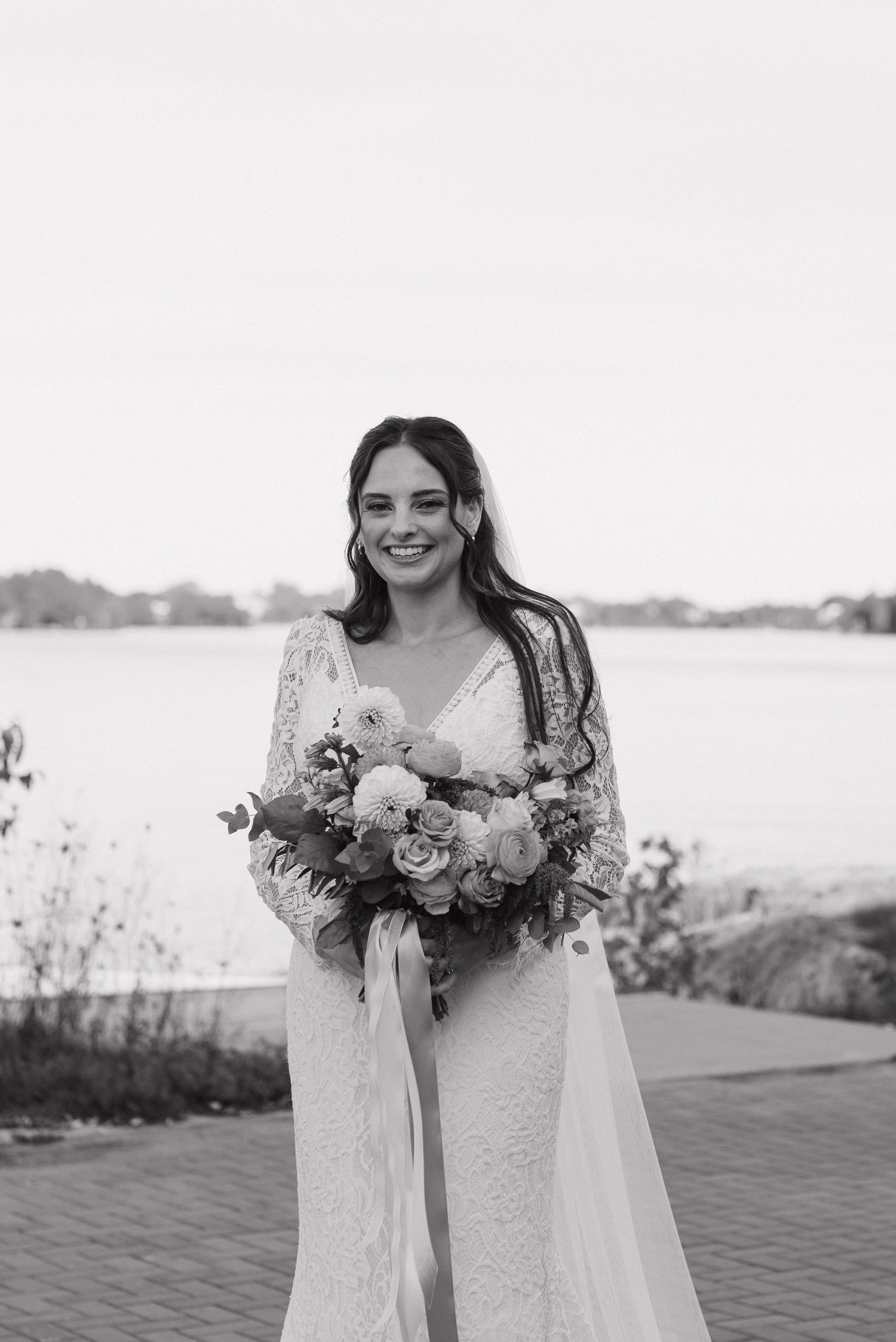 Bride holding beautiful peach and blush floral bouquet against waterfront backdrop.