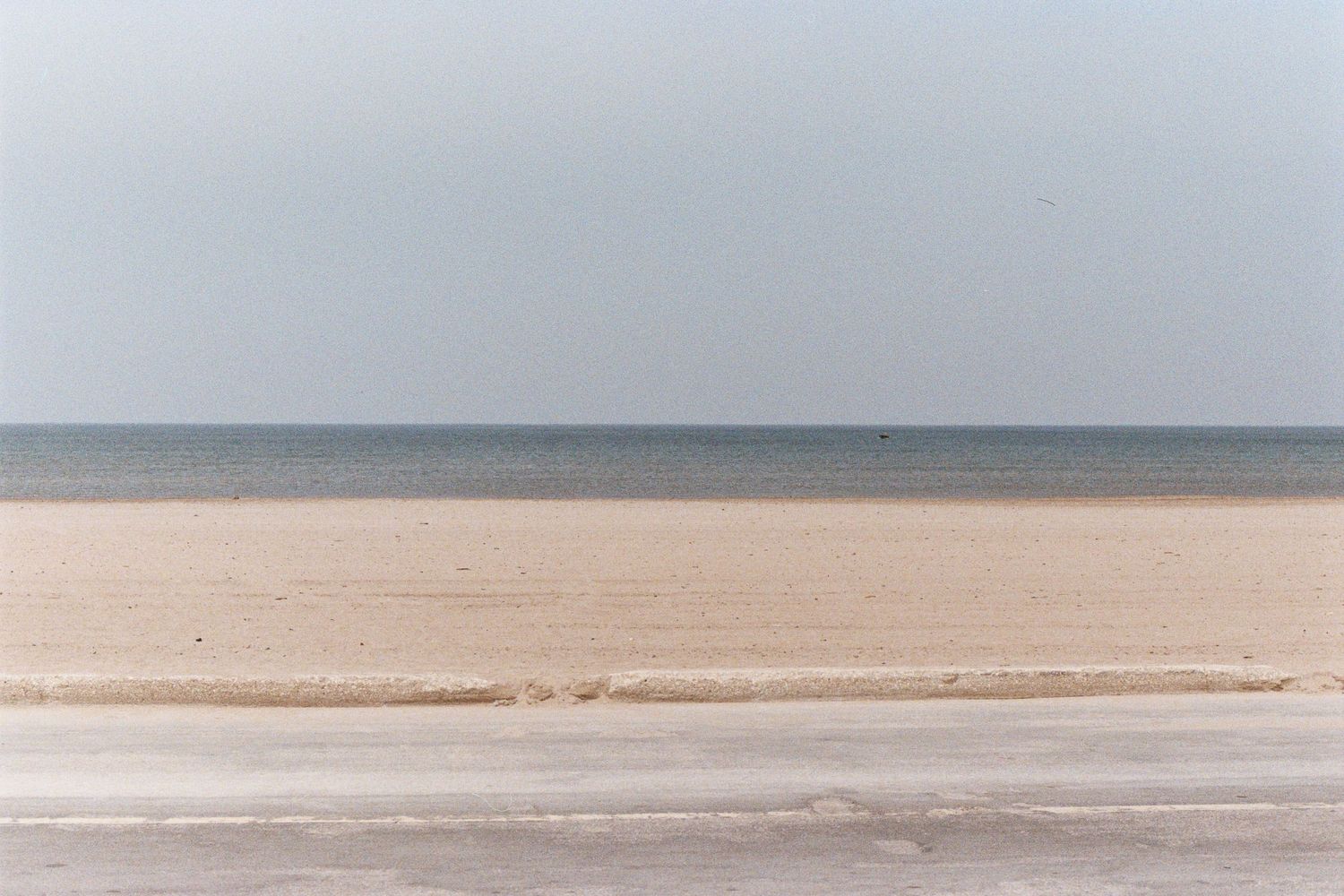 A scenic coastal beach landscape with gentle waves and sandy shores stretching to the horizon under a cloudy sky.