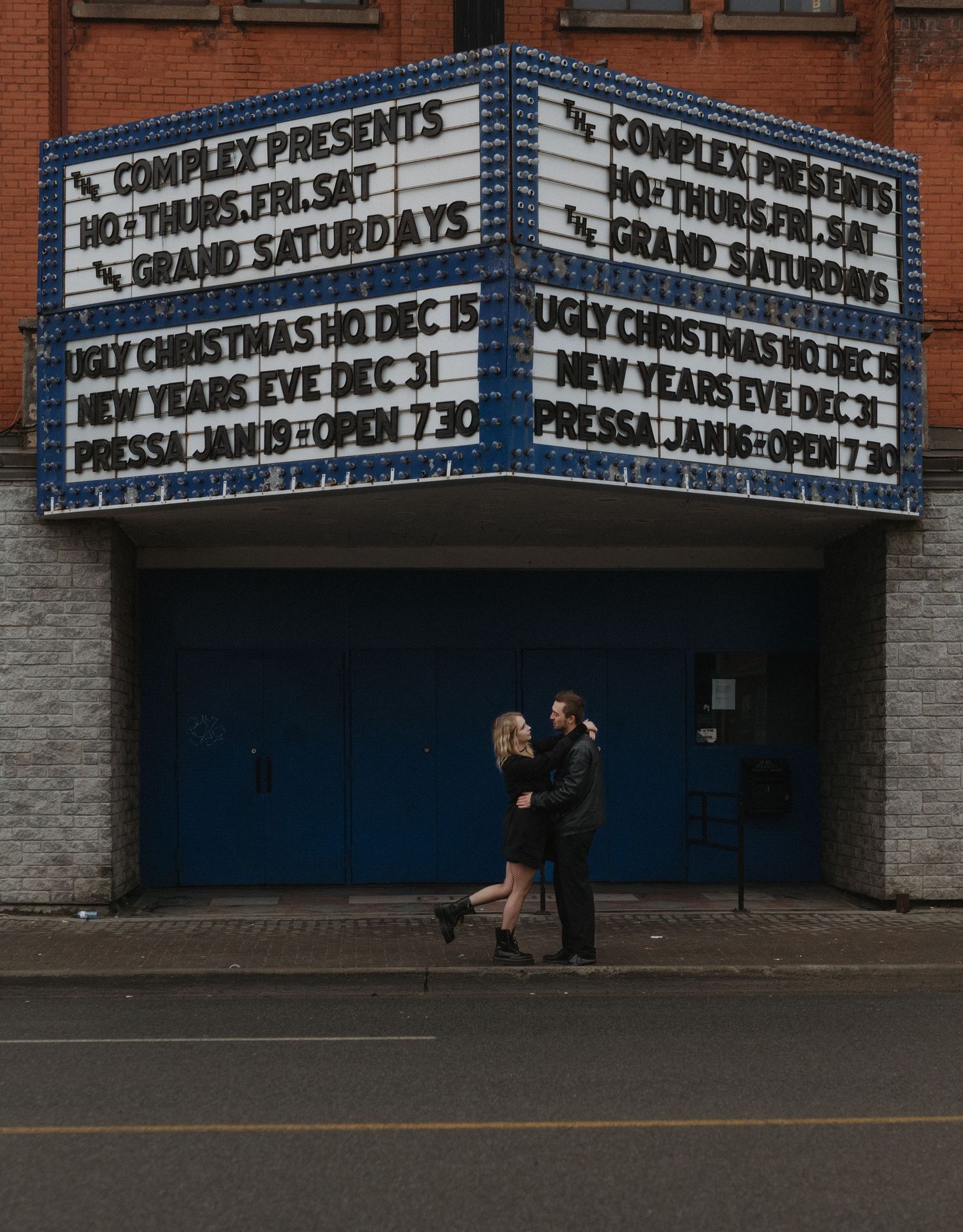 Movie theater marquee displays showtimes on a brick building exterior with blue trim and multiple panels.