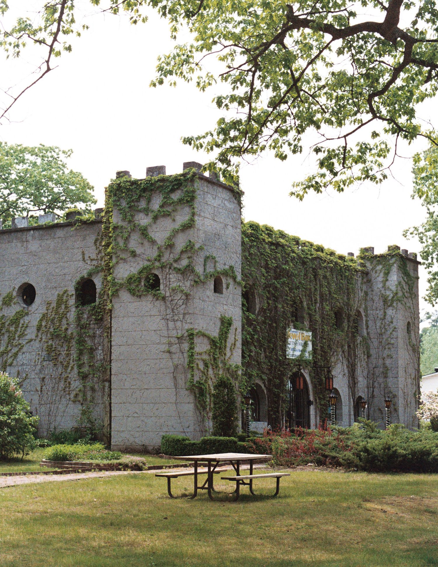 Abandoned stone building covered in ivy with arched windows and a picnic table in the foreground on grassy grounds.