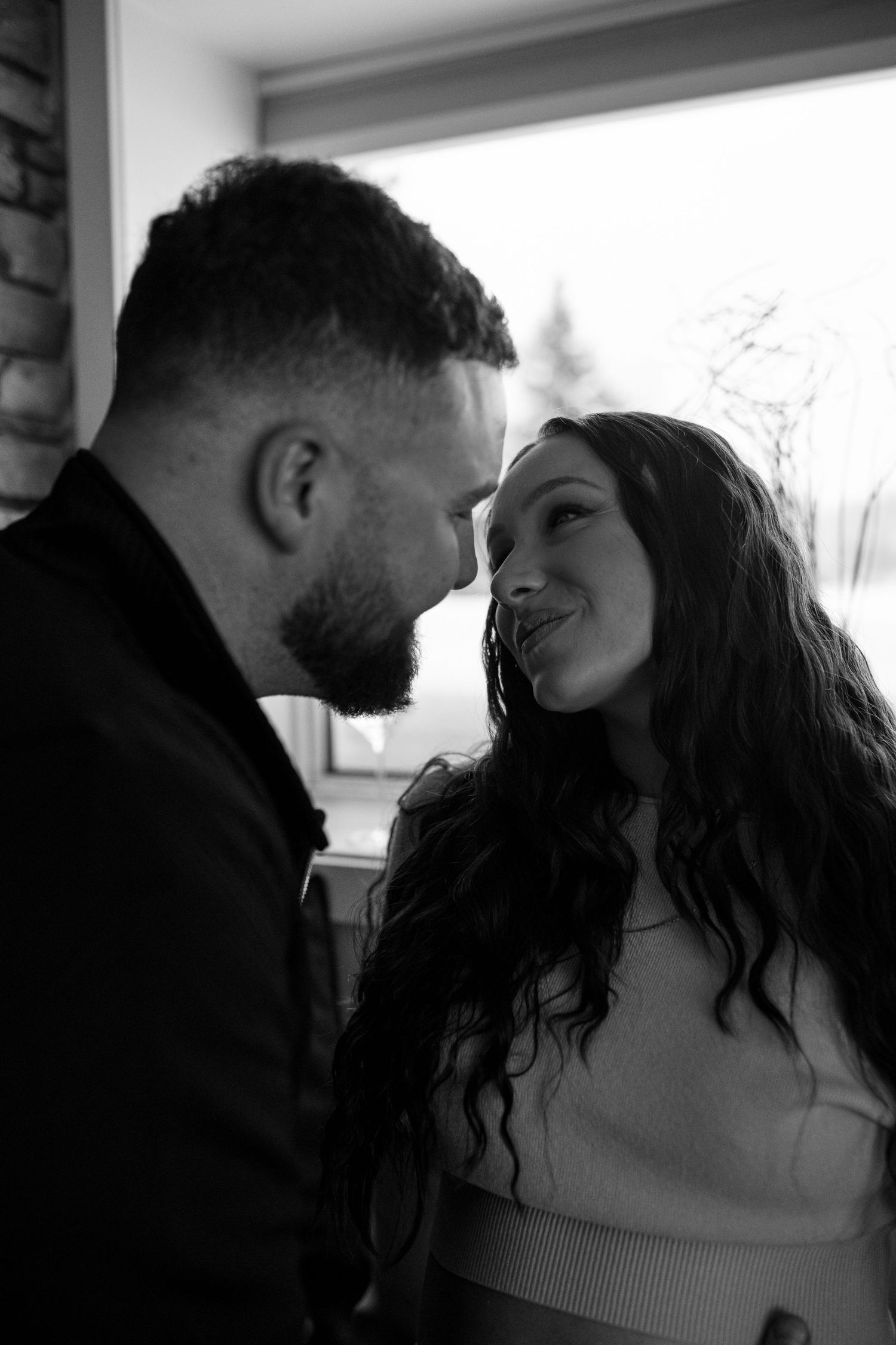 Couple shares a tender close moment together, nearly touching foreheads in a romantic black and white portrait photo.