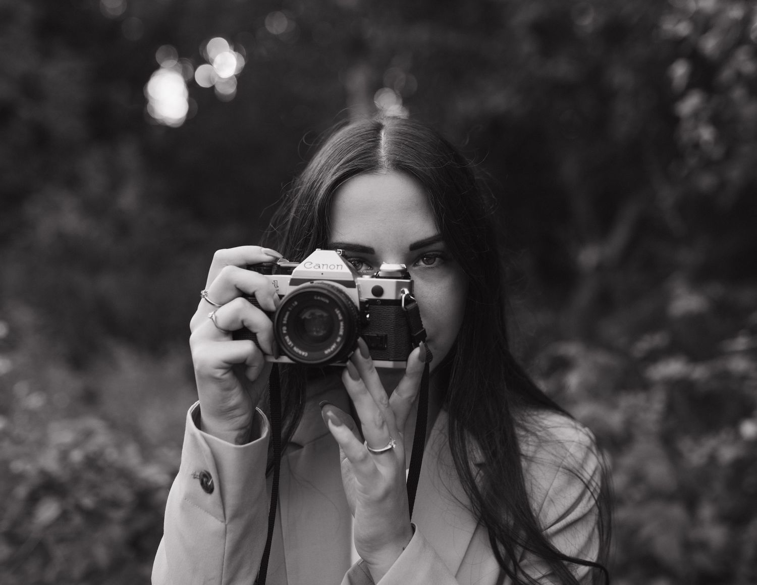 Black and white image of someone holding a vintage camera while taking a photograph outdoors.