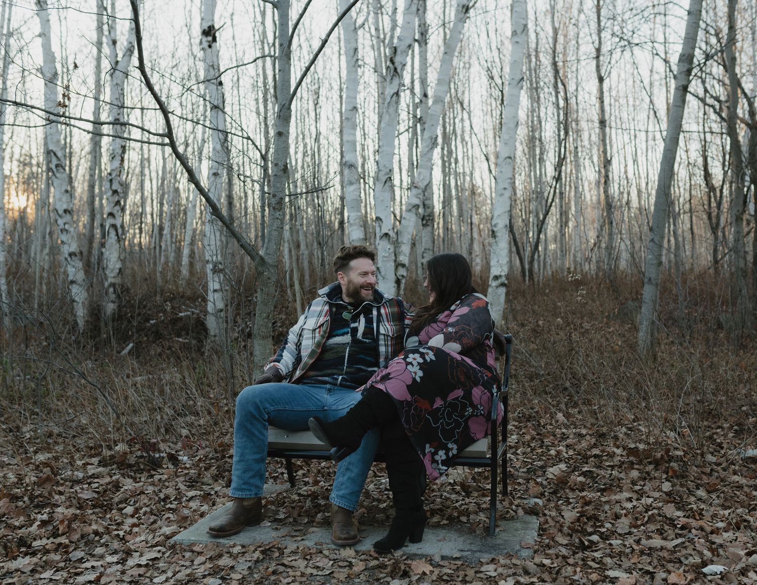 A group sits on fallen leaves in an autumn forest with bare trees stretching into the distance.
