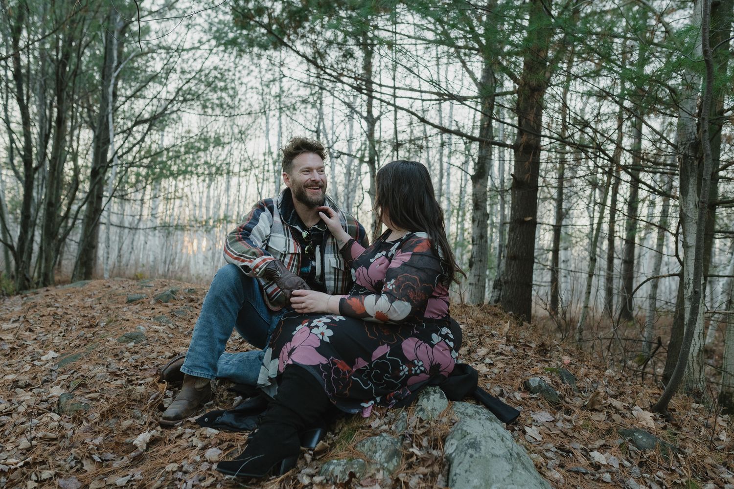A couple sits together on fallen logs in a misty autumn forest during a romantic outdoor photoshoot.