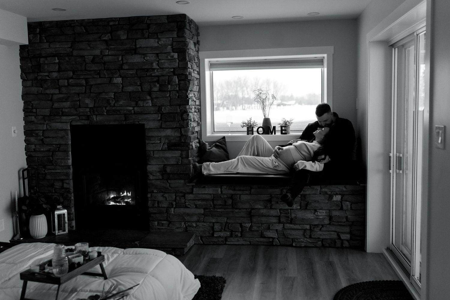 Black and white photo of couple in modern home with stone fireplace.