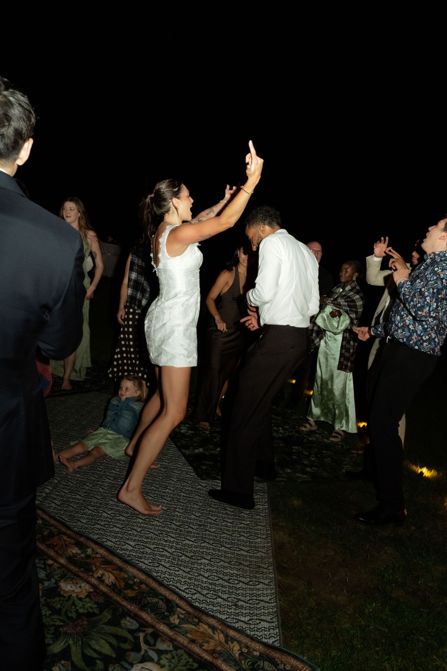 Bride in white mini dress dancing with groom at outdoor wedding reception at night.