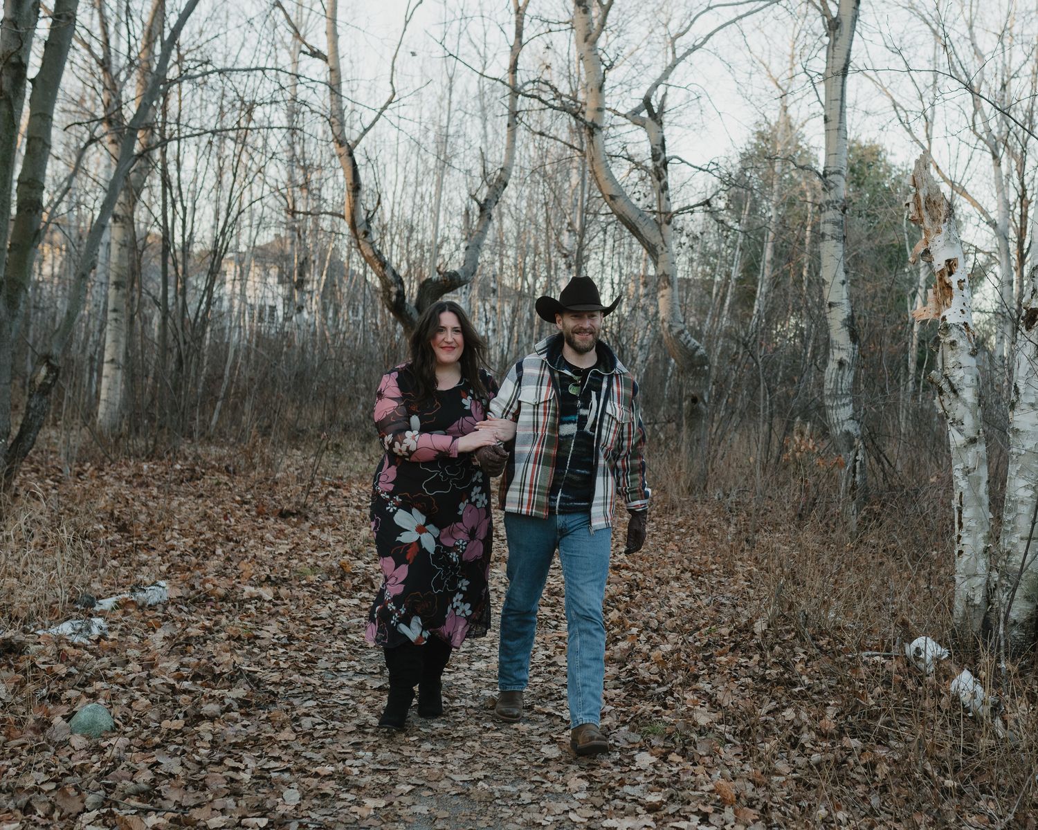 A family walks through a serene winter forest with bare trees and fallen leaves covering the ground.