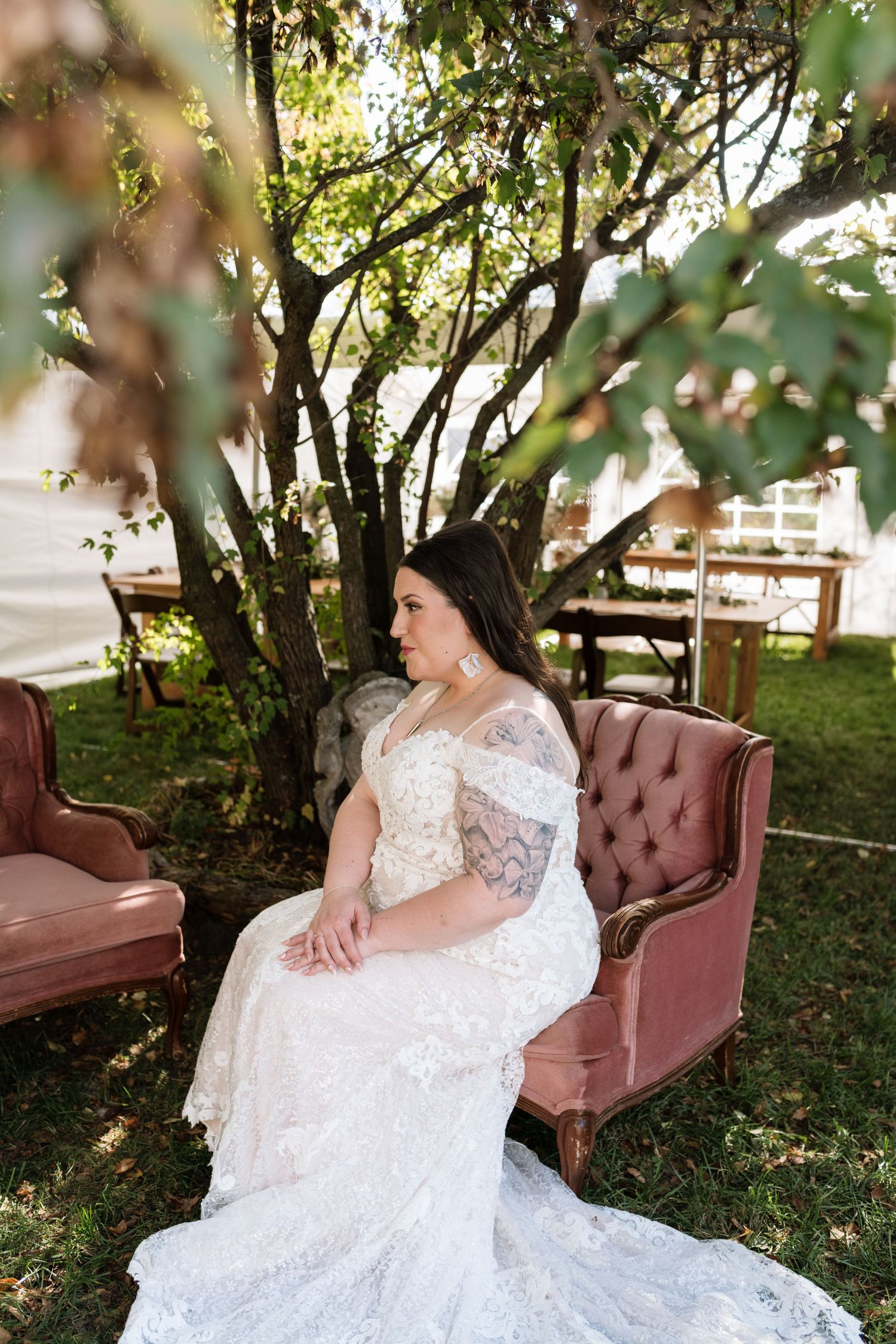 A wedding dress with lace details spread elegantly across a vintage brown velvet settee in a garden setting.
