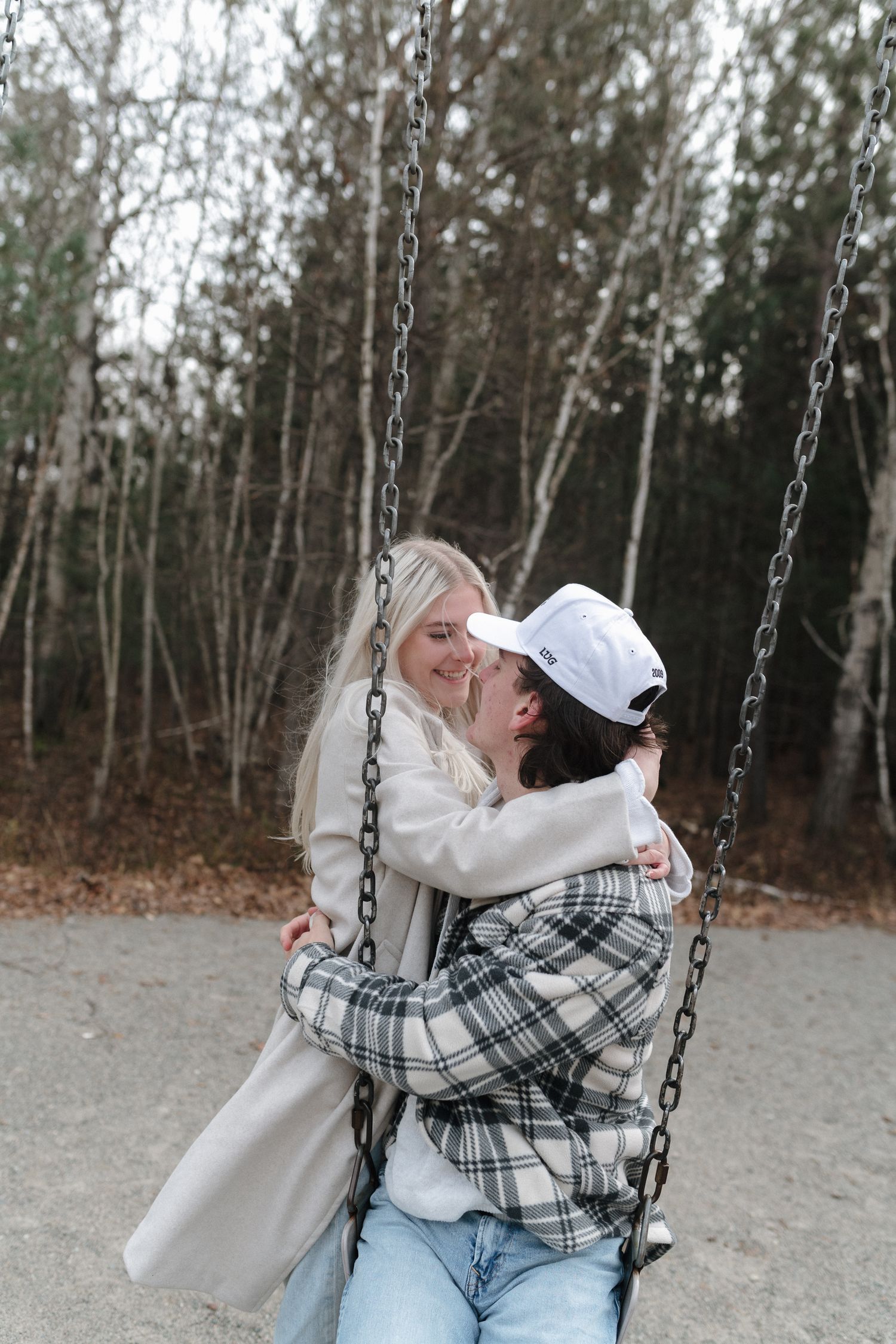 Couple sharing a romantic moment on a swing set, surrounded by bare autumn trees.