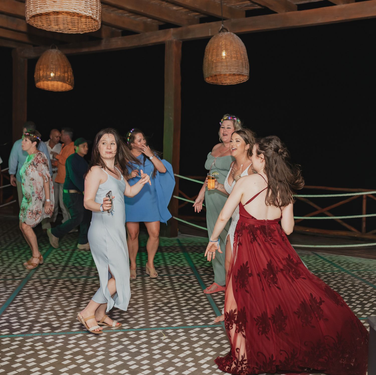 Couples dancing together on a patterned floor at an evening event with woven pendant lights overhead.