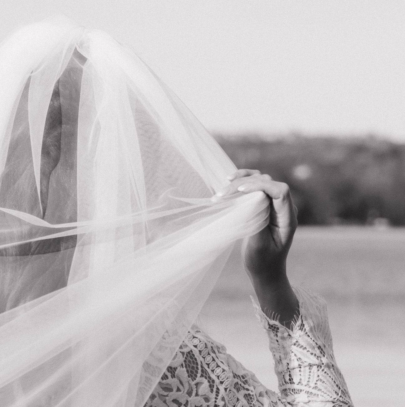 Bride in a white veil and lace dress poses in a black and white outdoor photo series.