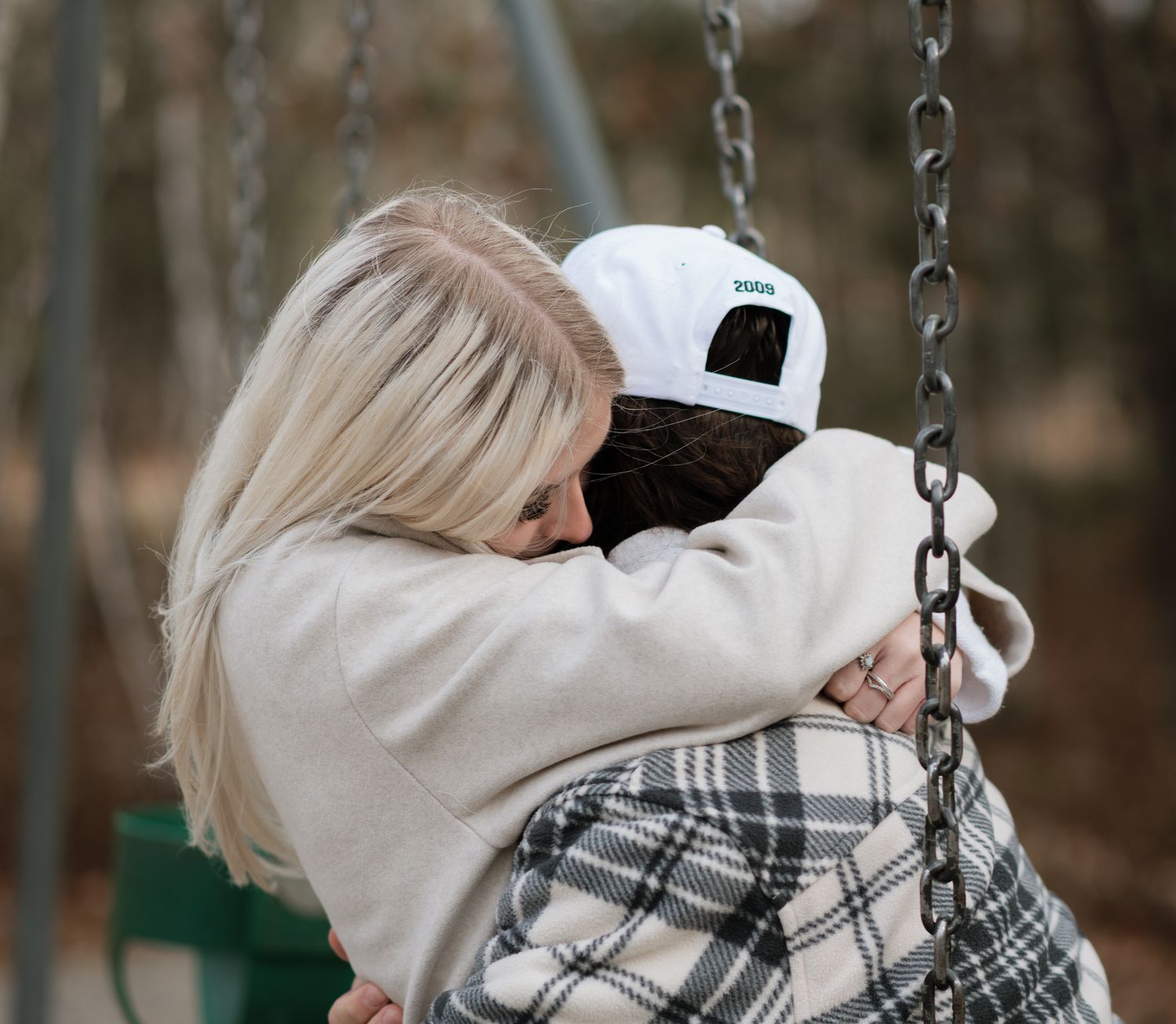 Couple sharing a warm embrace on a playground swing surrounded by fall foliage.