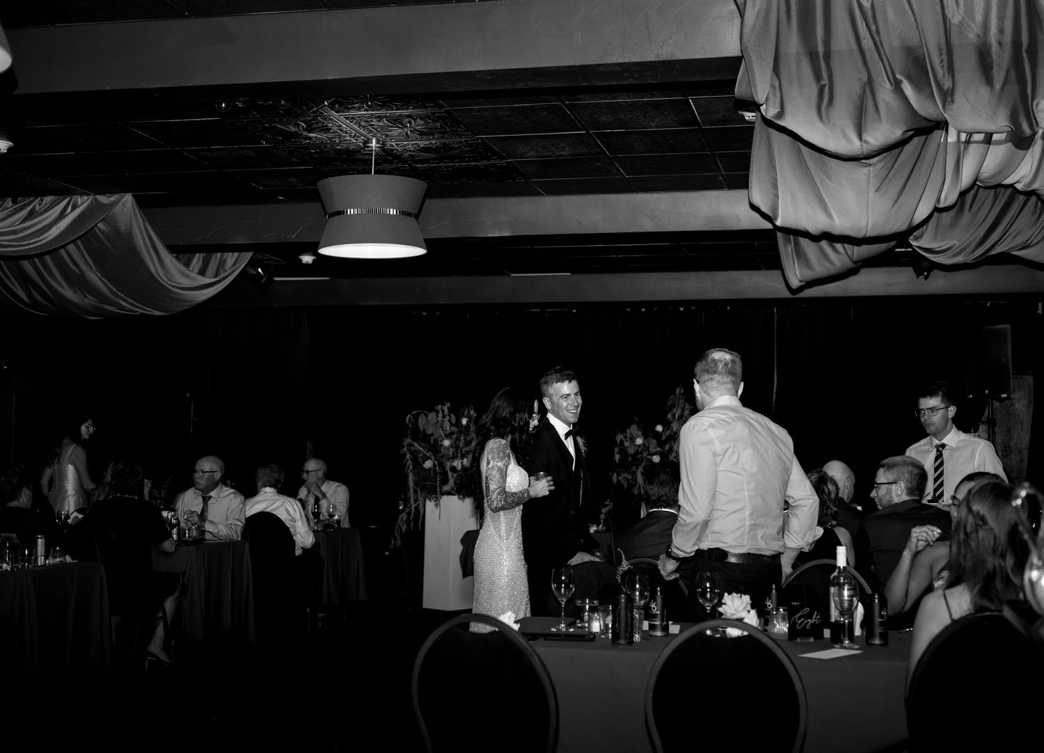 Black and white photo of elegantly dressed guests dining at a formal banquet event in a decorated restaurant.