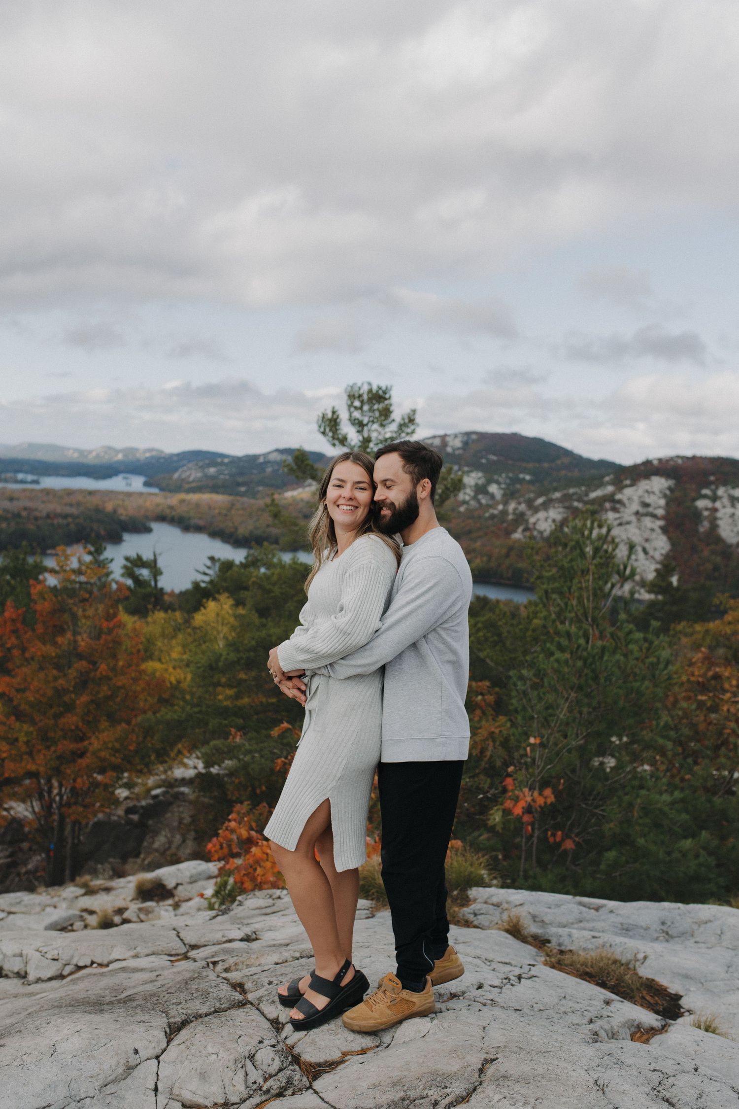 A couple embracing on a rocky overlook with autumn foliage and mountains in the background.