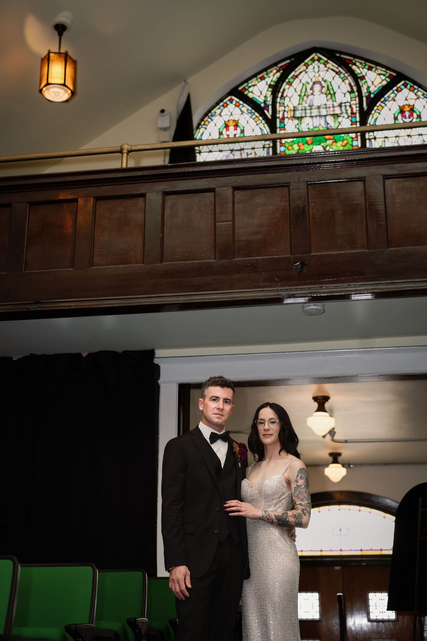 Elegant couple in formal attire posing in a church with stained glass windows and wooden balcony.